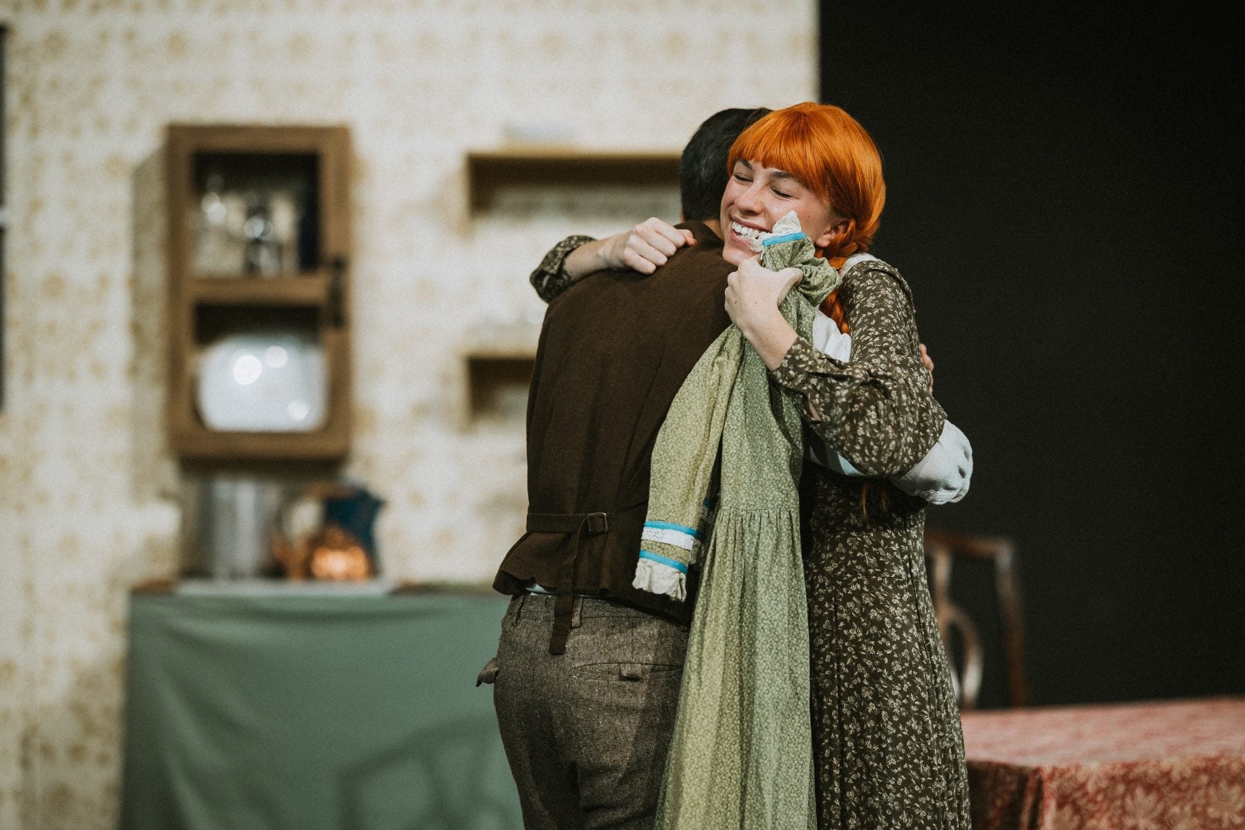 Two actors embrace warmly in a home-set scene during the school play