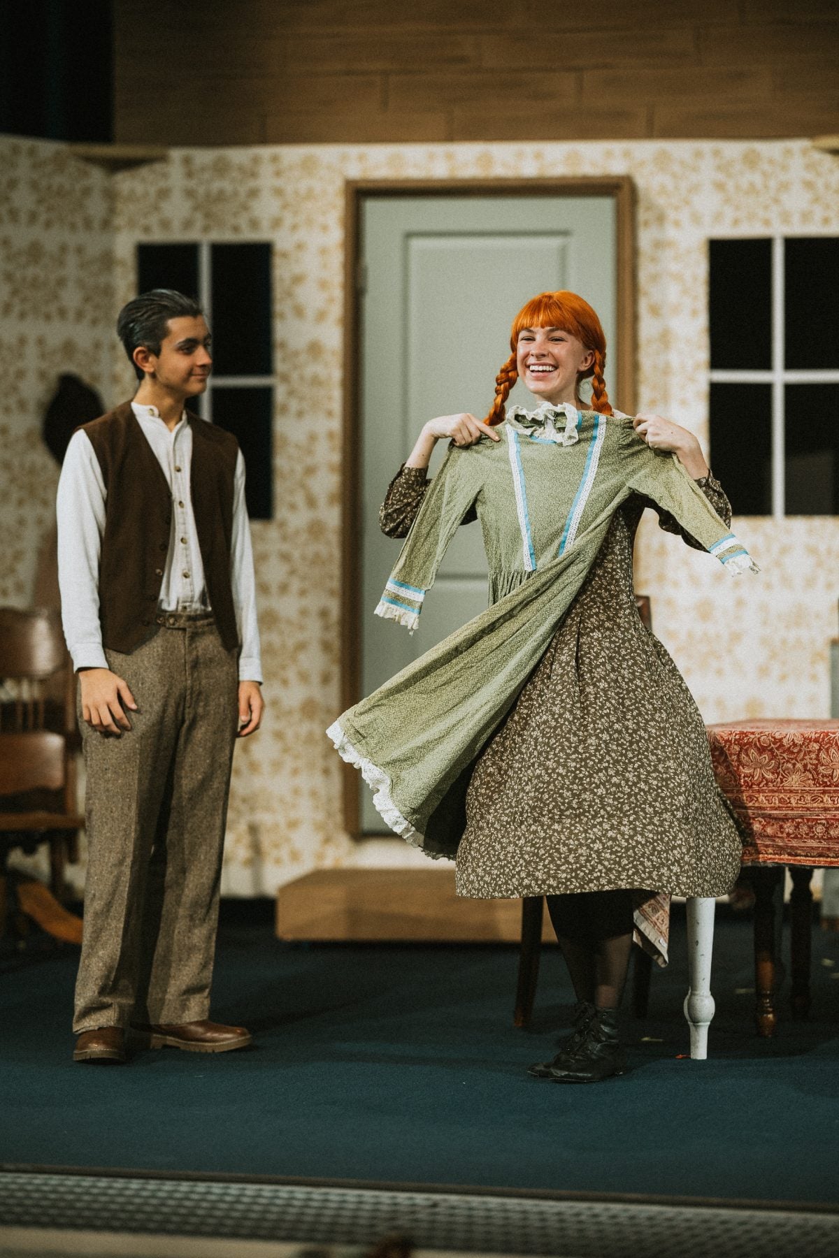 Two students share a lighthearted moment over a green dress on stage