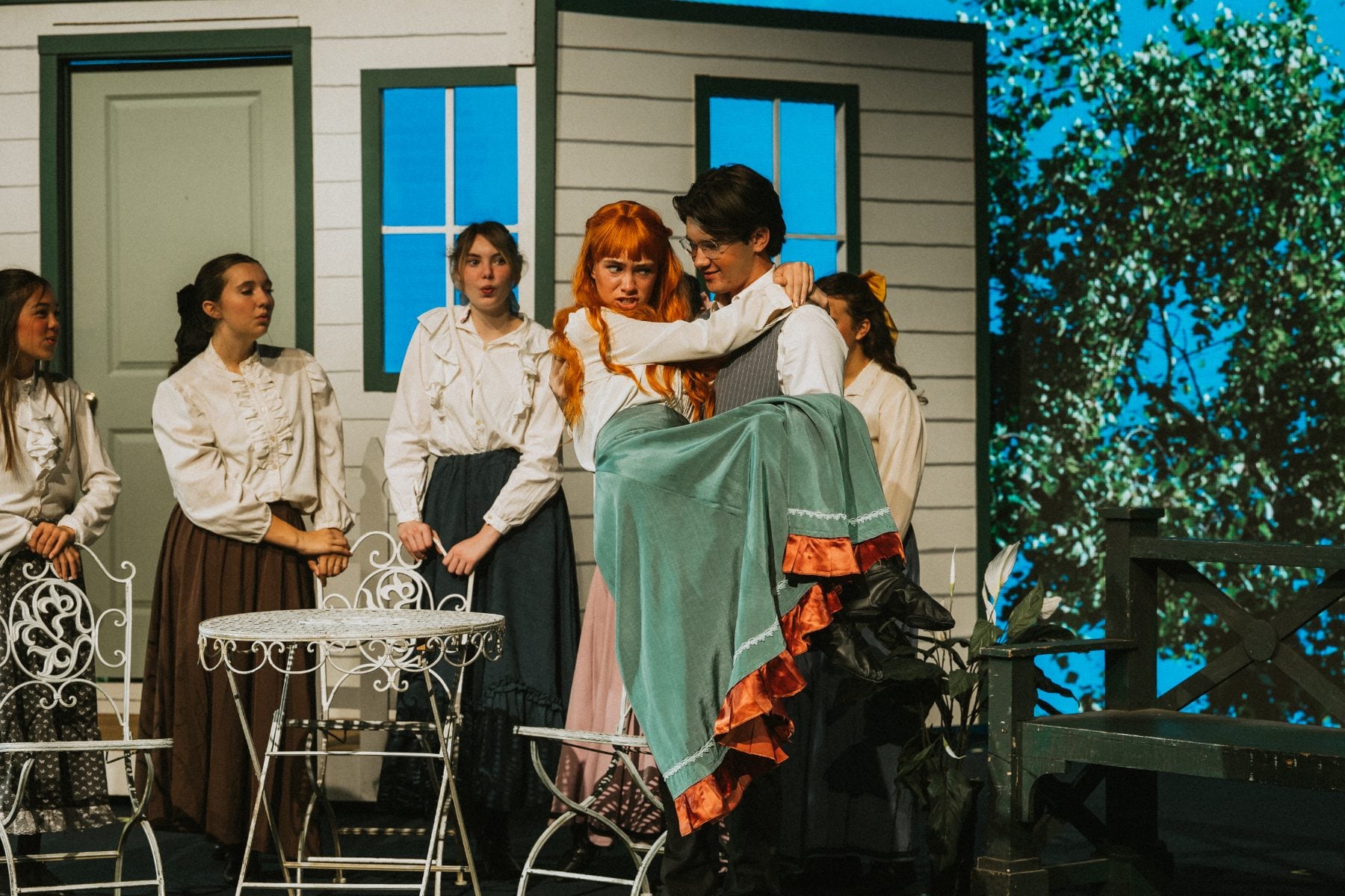 A group of students comfort a red-haired classmate in an outdoor set scene