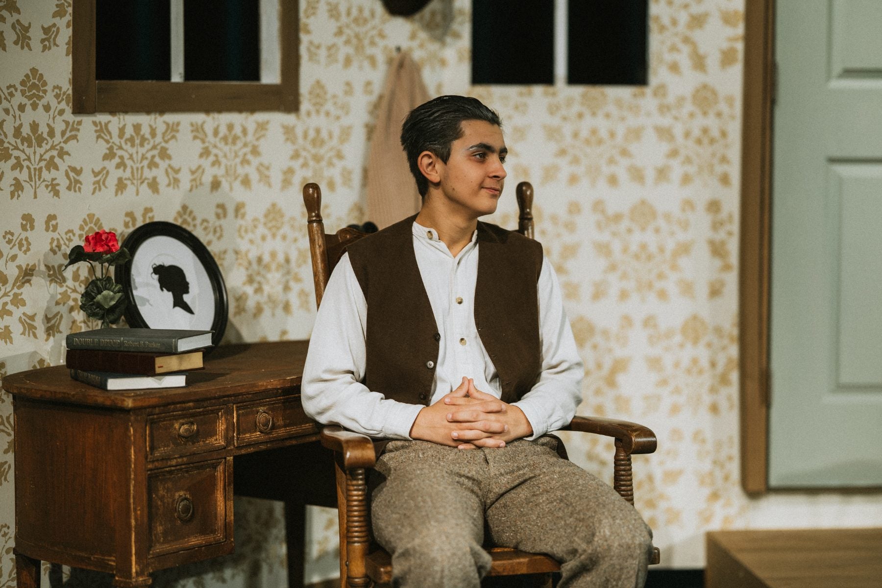 A student sits thoughtfully in a vintage-style room during the school play