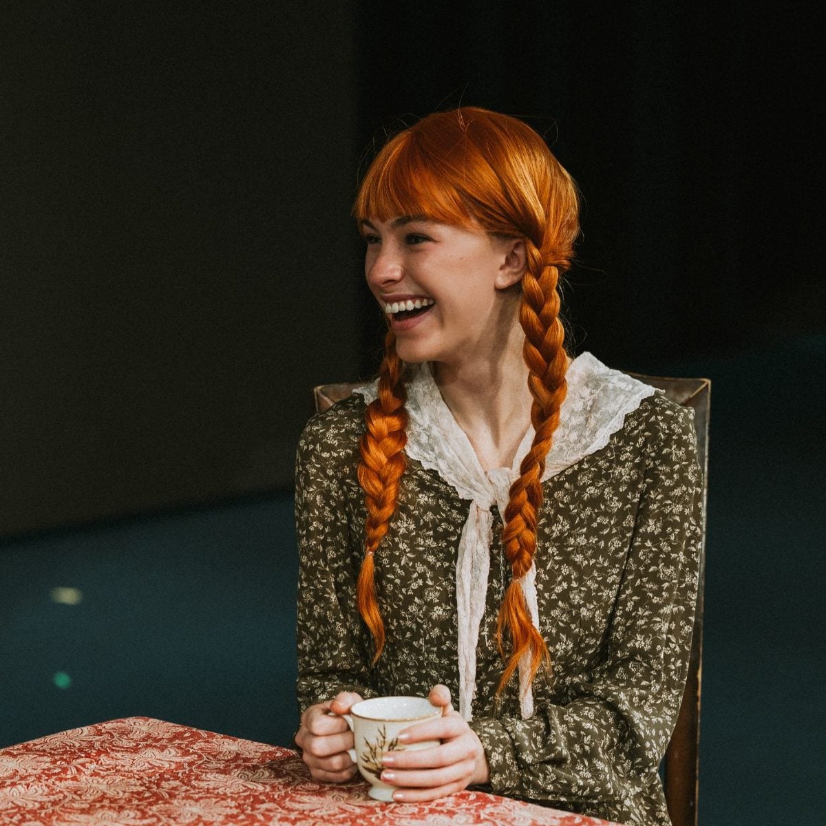 A student in red braids laughs while holding a teacup during the performance
