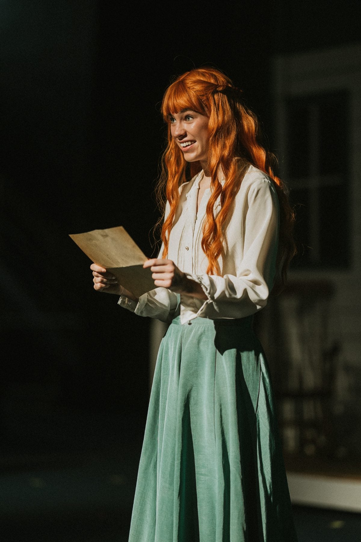 A student with red braids reads a letter in the Anne of Green Gables play