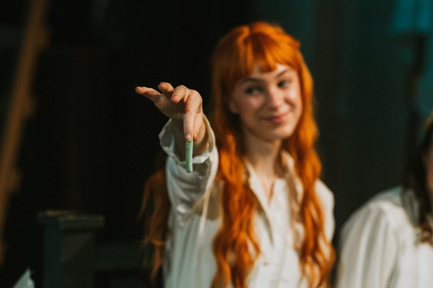 A student with red braided wig holds up a small charm, smiling on stage