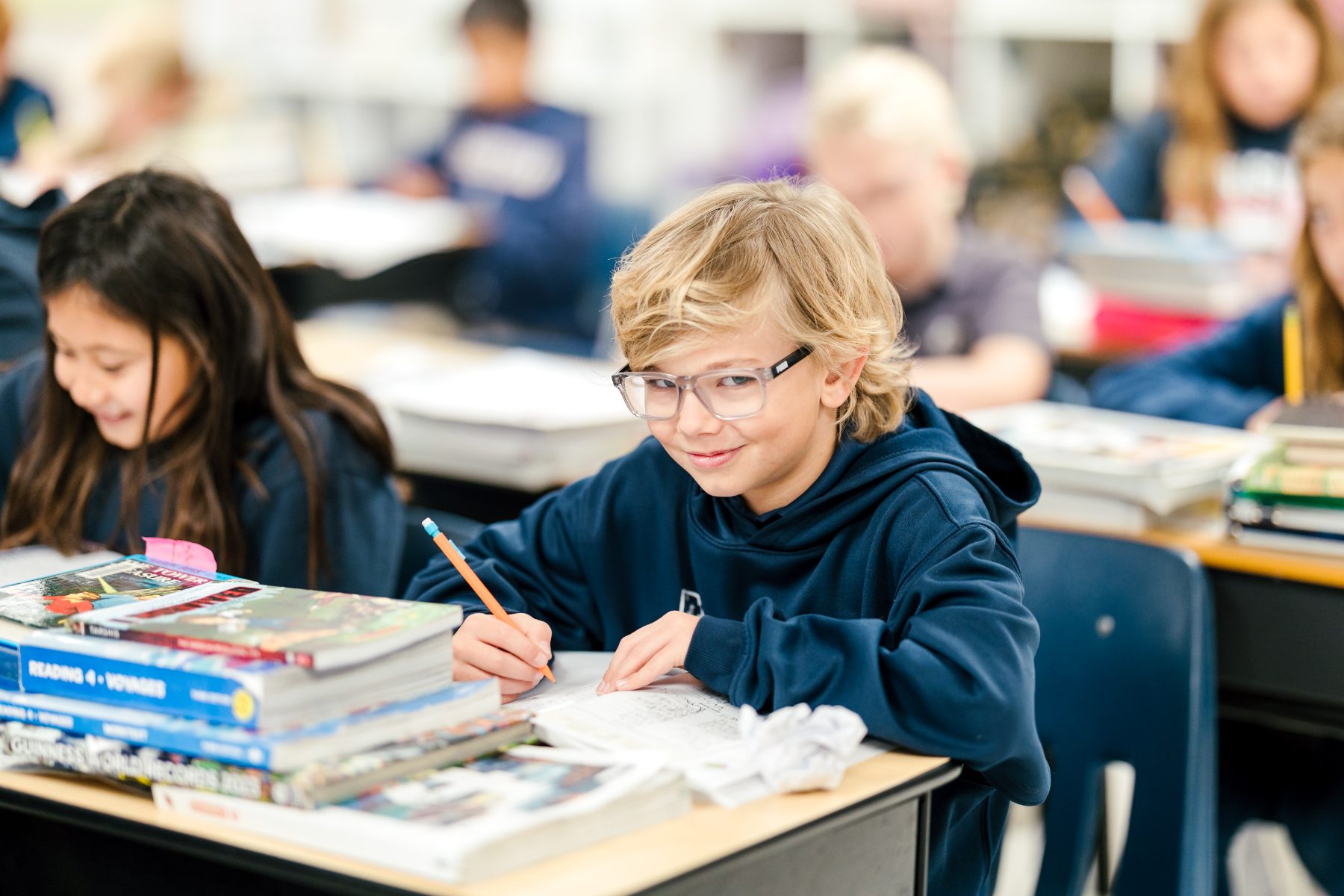 A student in glasses writes in his notebook during class at his desk