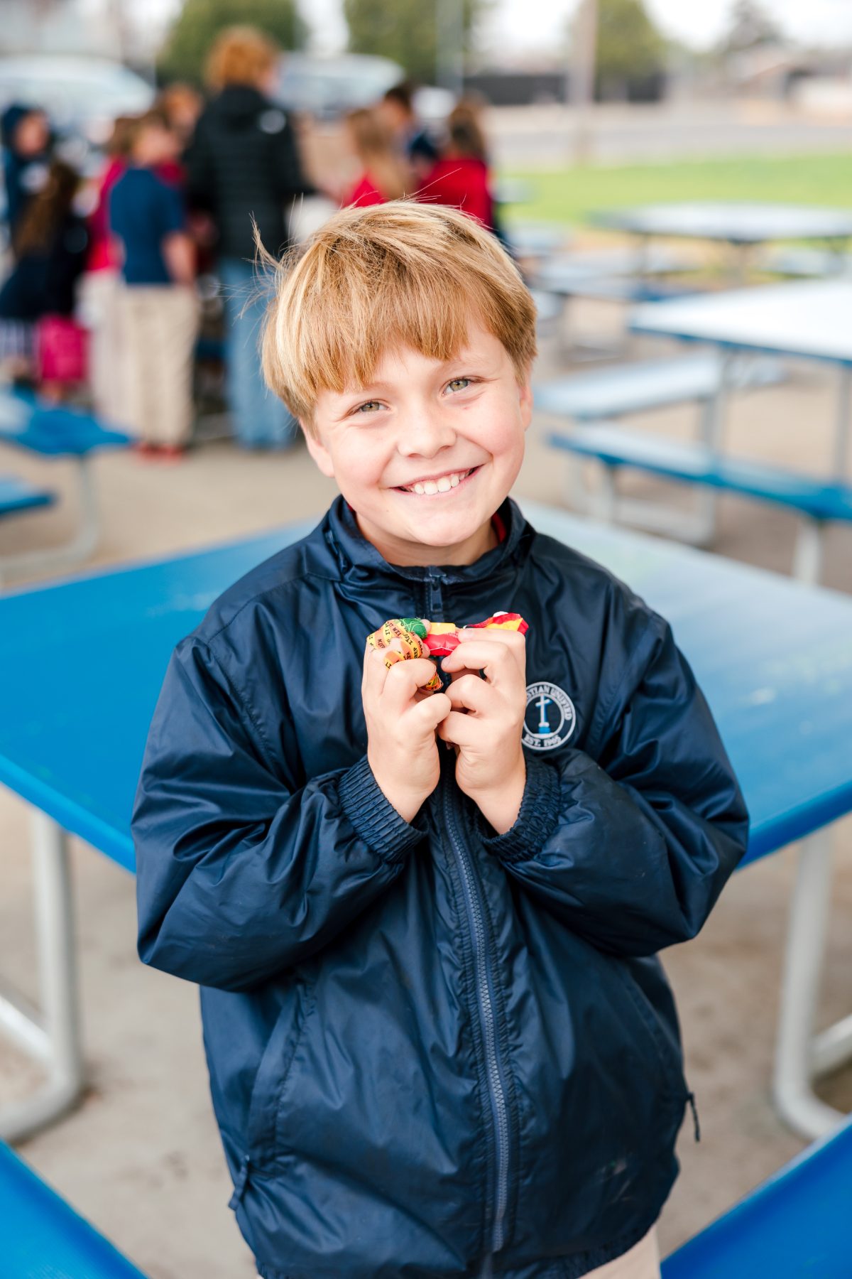 A boy in a navy jacket holds a snack at an outdoor picnic table