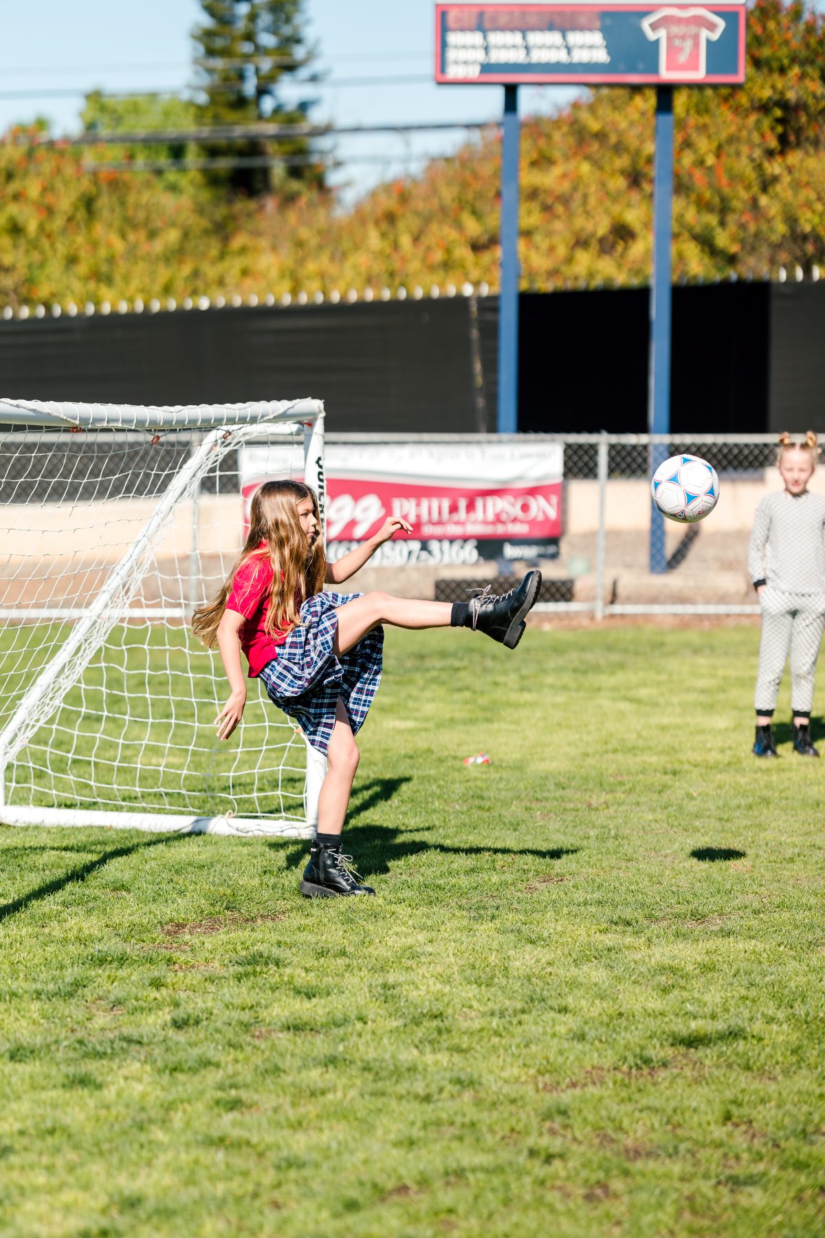 A girl kicks a soccer ball toward the goal as a boy watches
