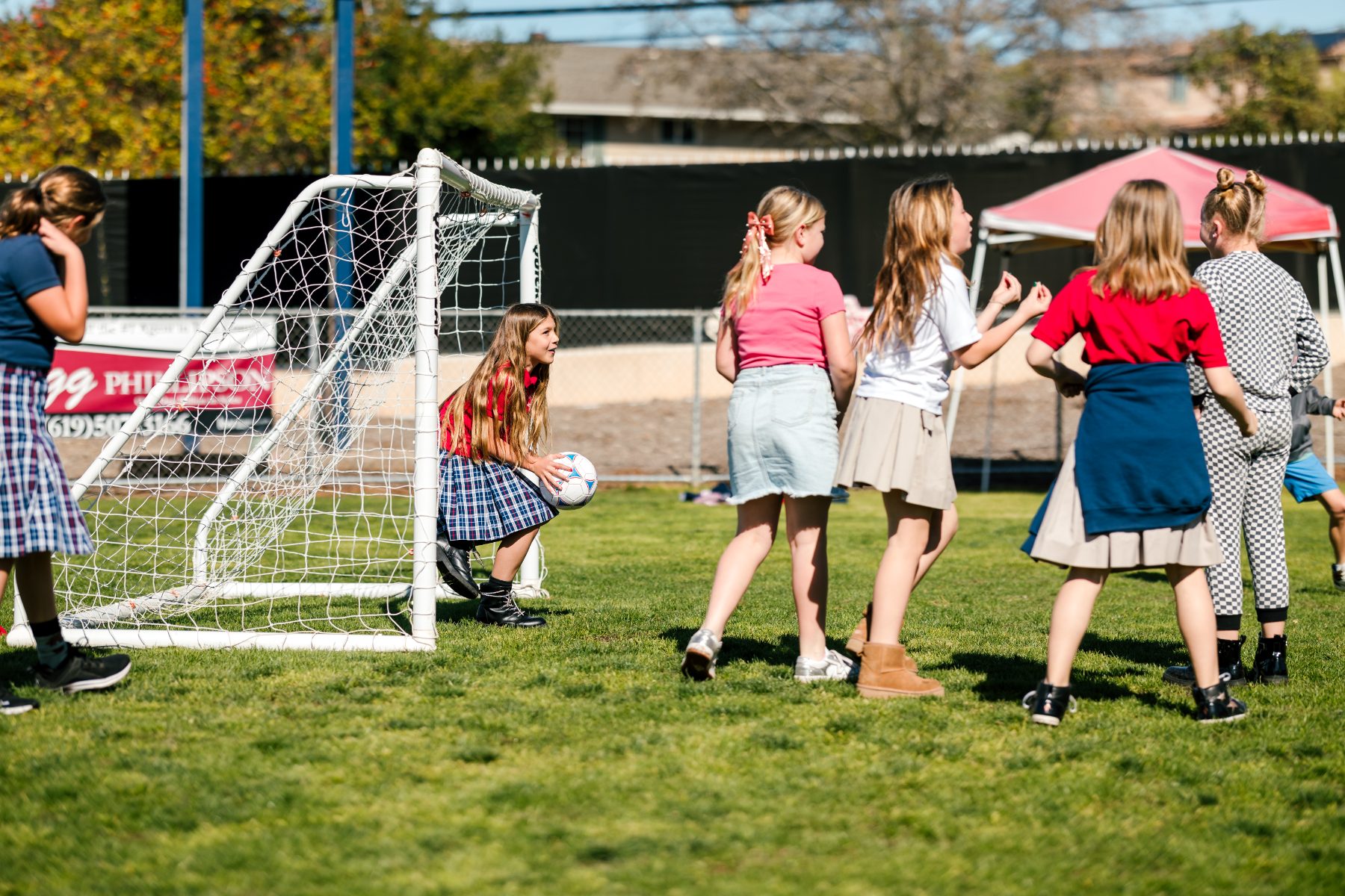 Girls gather around the goal as one kneels with the ball