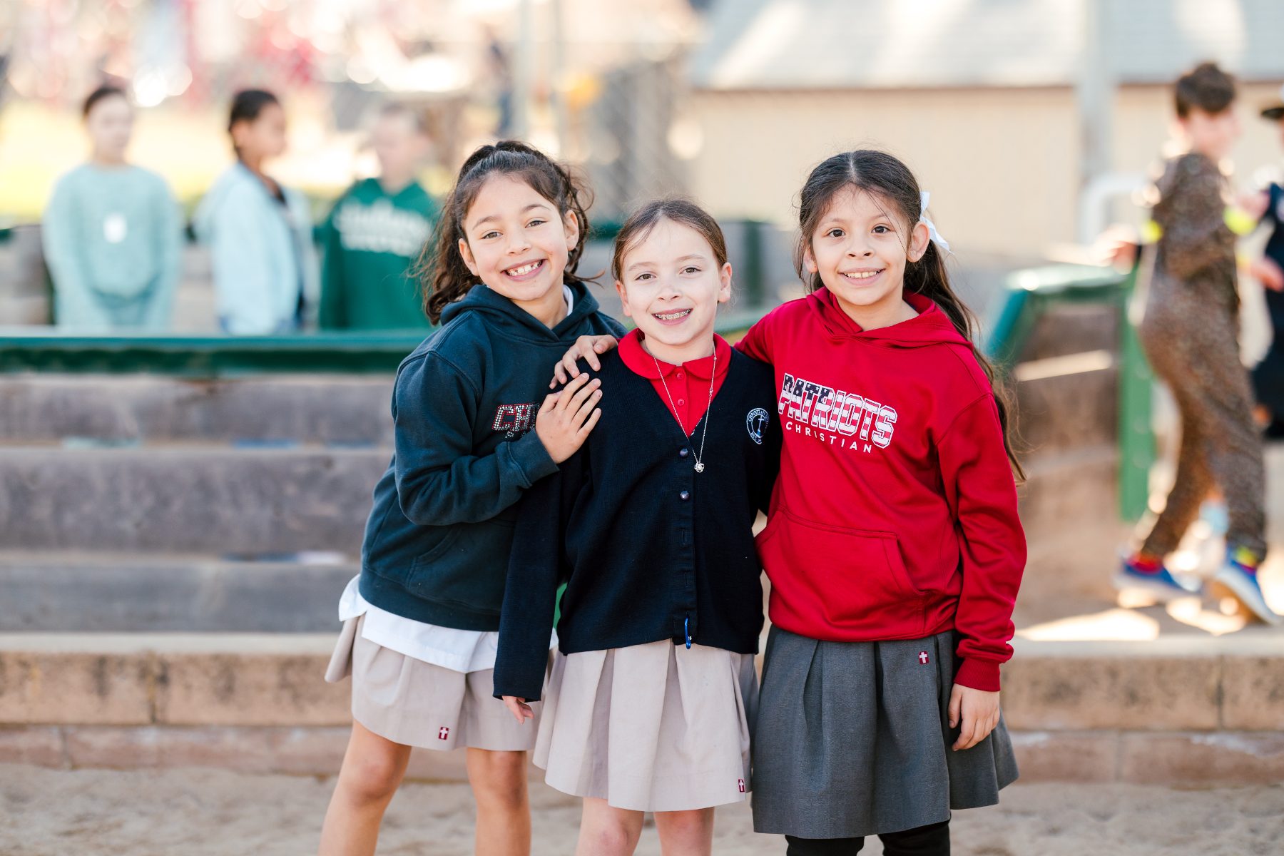 Three girls stand close together laughing on the campus playground