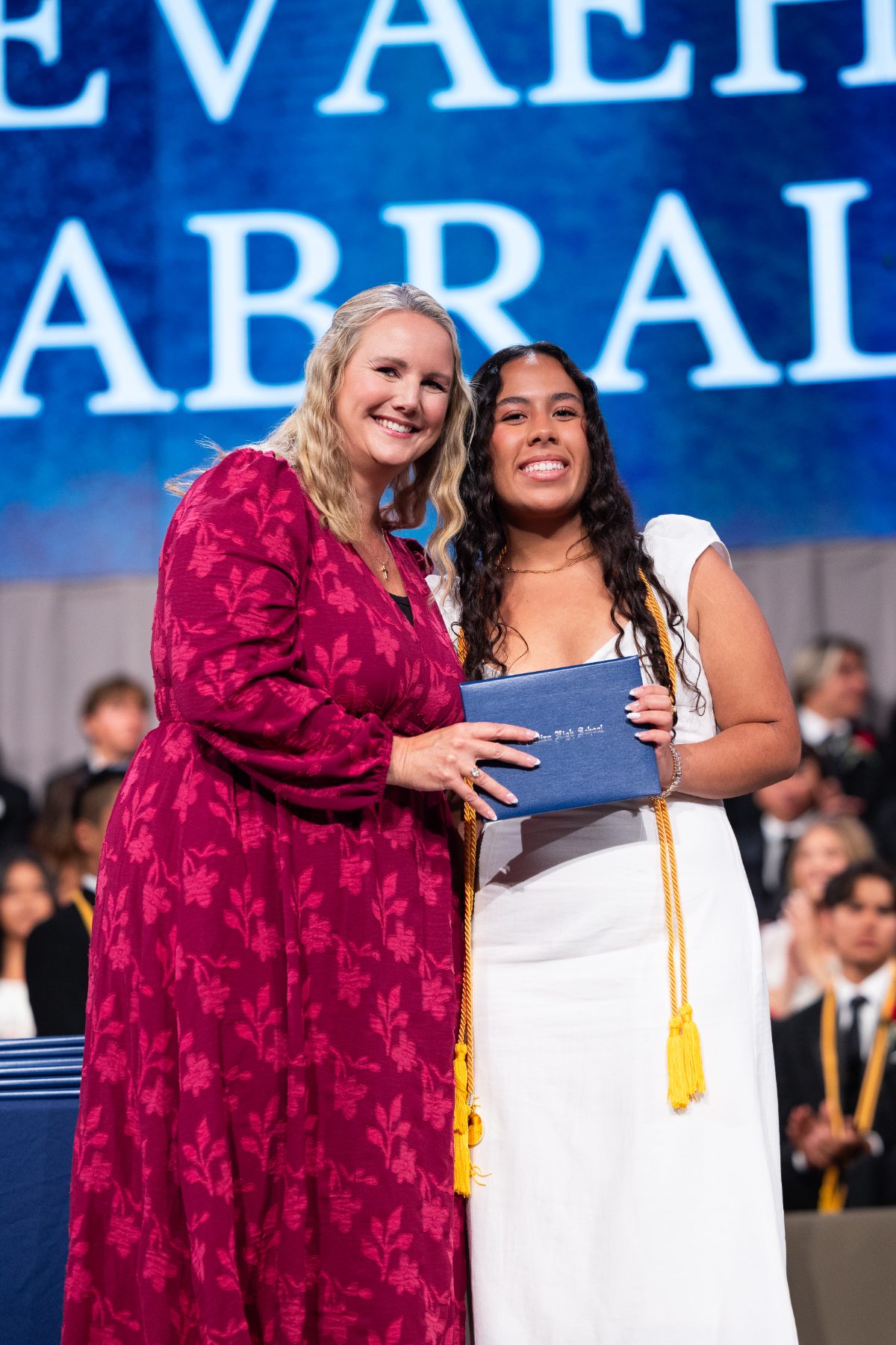 A staff member presents a diploma to a graduate named Evaeh on stage