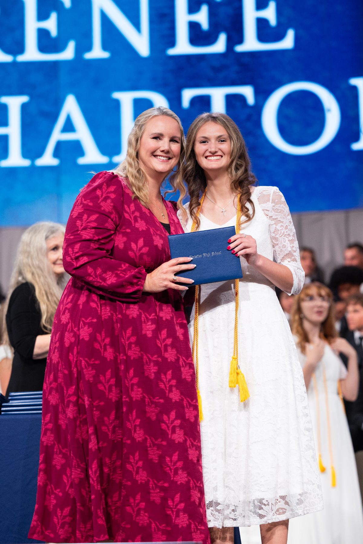 A staff member hands a diploma to a graduate in white at commencement