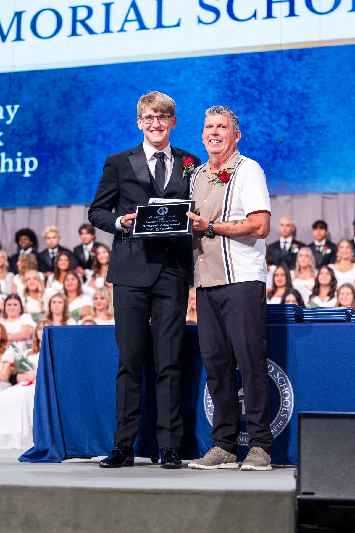 A student receives a plaque from a man on stage during the scholarship ceremony