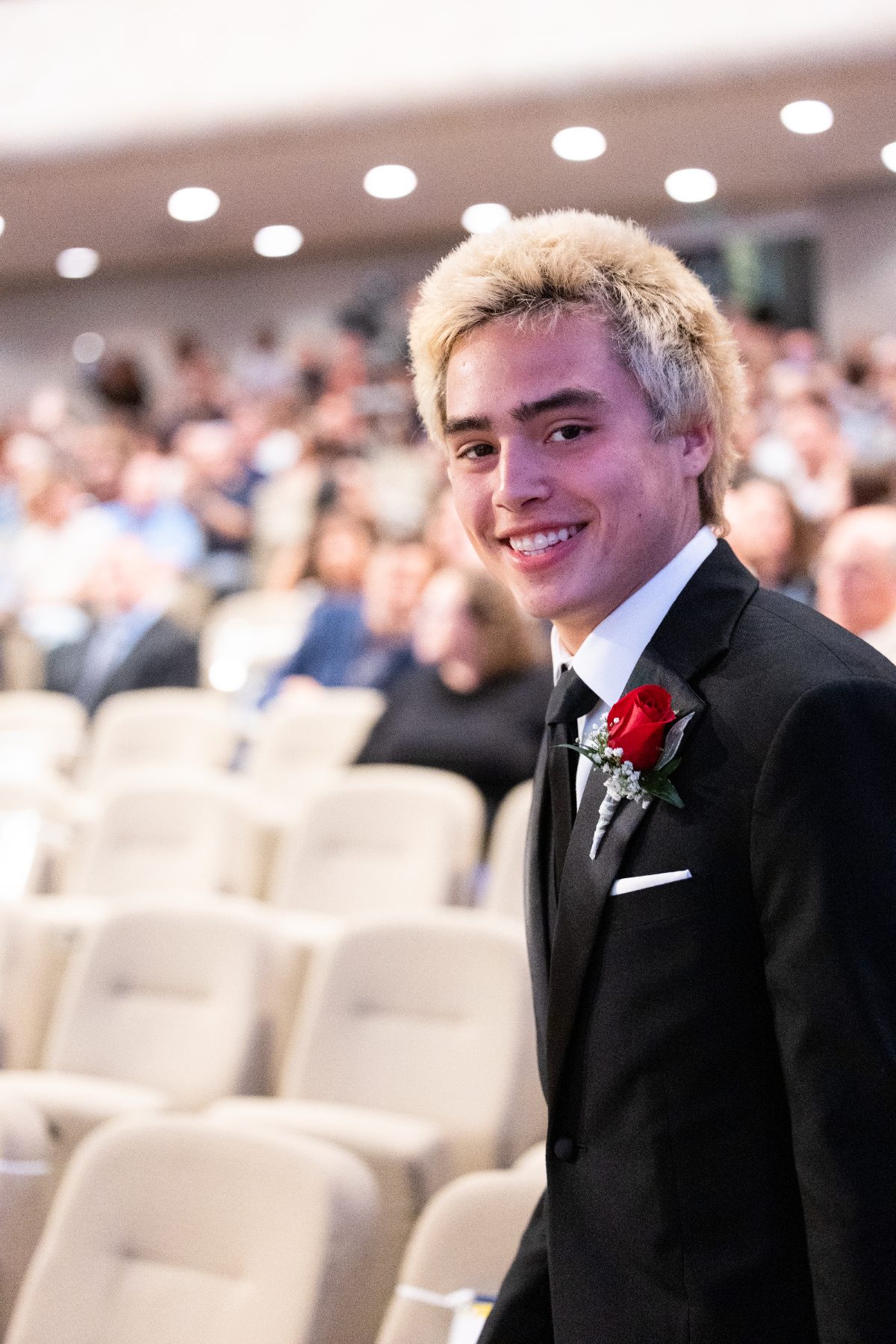 A student smiles in the audience wearing a boutonniere before commencement
