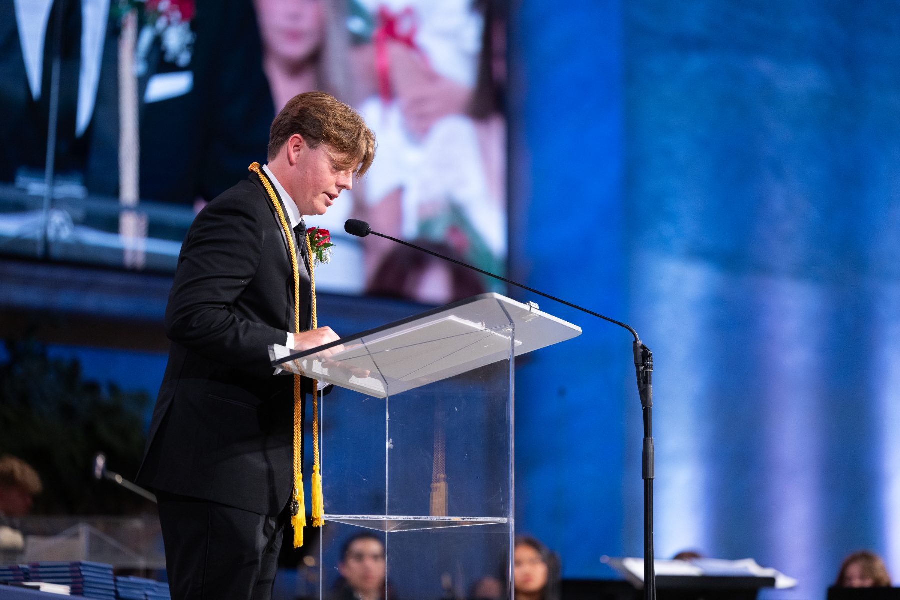 A graduate speaks at the podium wearing an honor cords stole