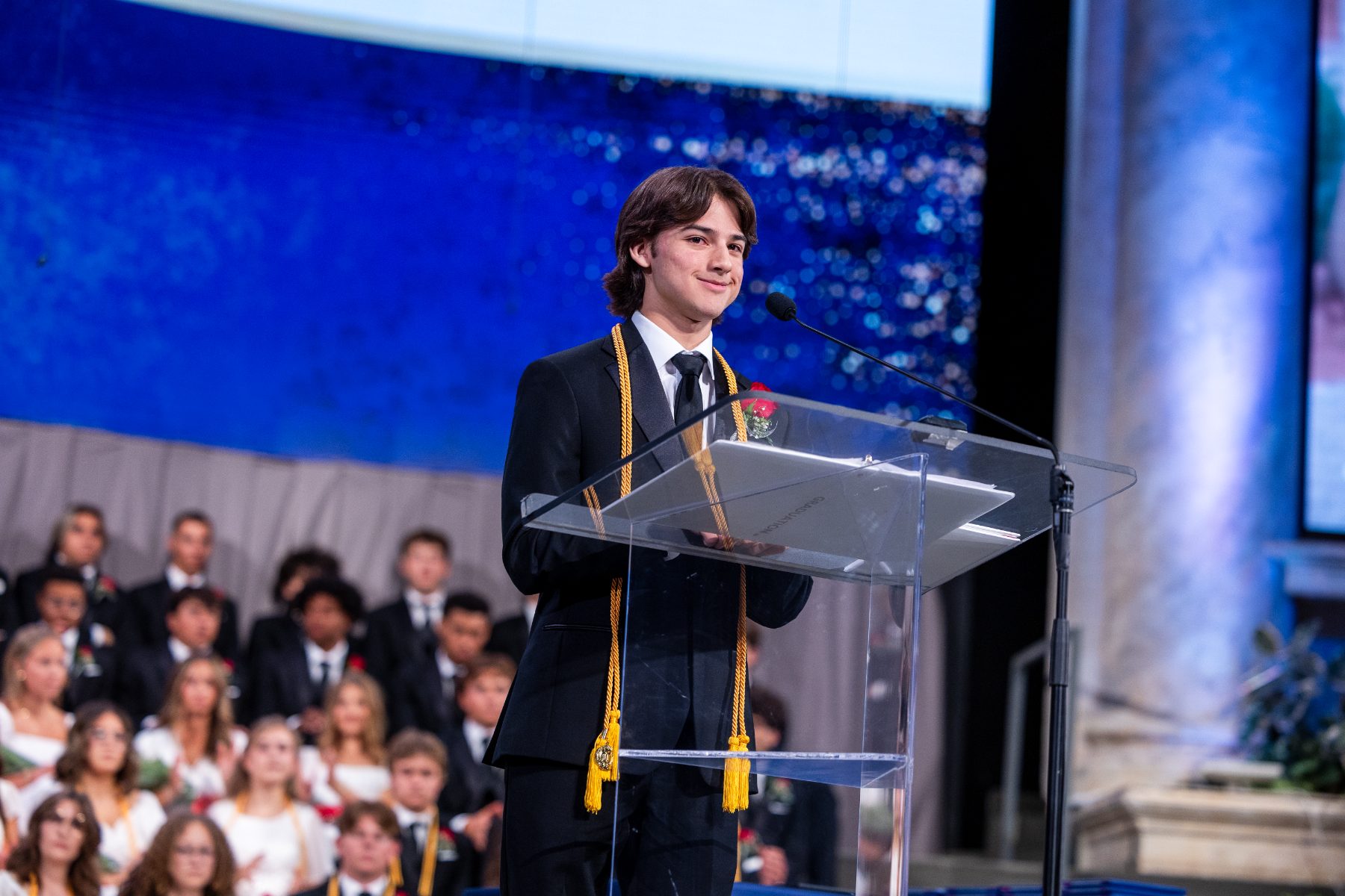 A student in honor cords speaks at the podium during commencement