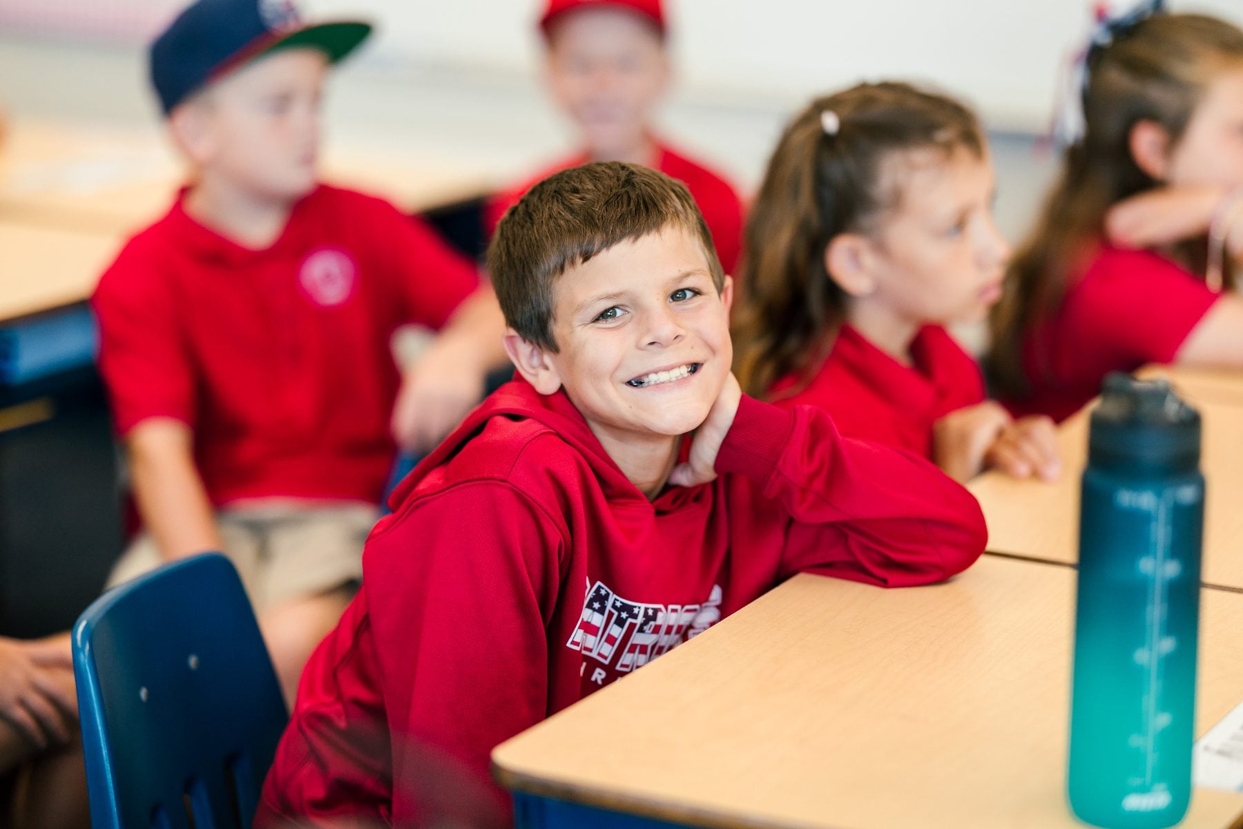 A young boy smiles at his desk during class at a Christian elementary school