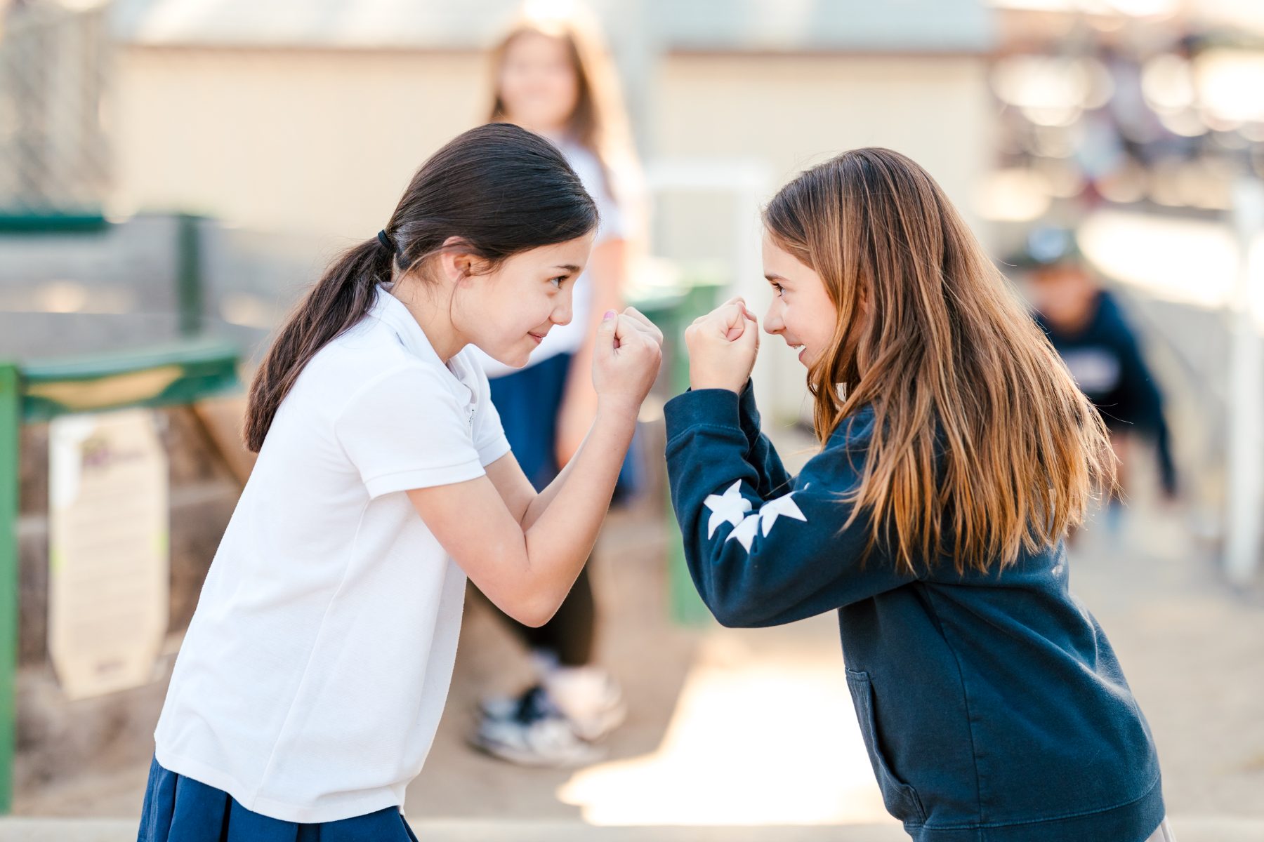 Two girls bump foreheads playfully outside on campus