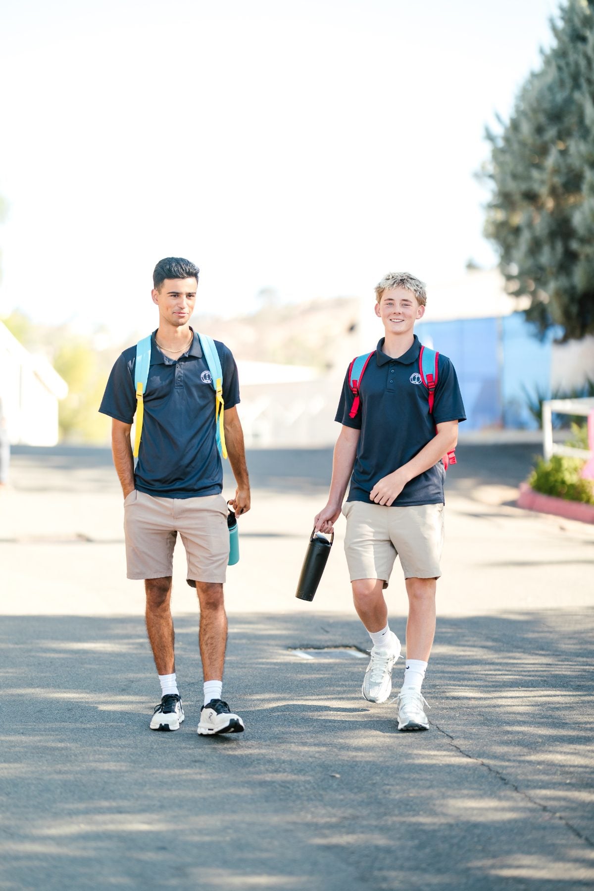 Two high school boys walk to class carrying backpacks and water bottles