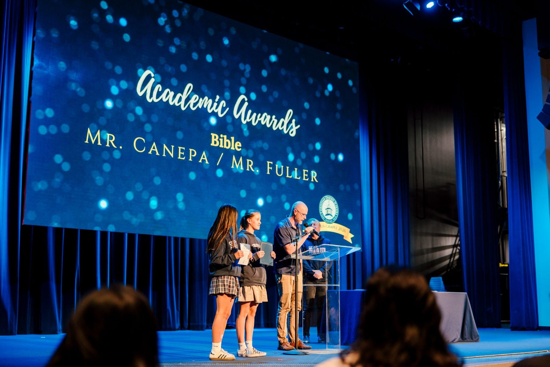 Presenters stand under a screen reading Academic Awards Bible at the ceremony.
