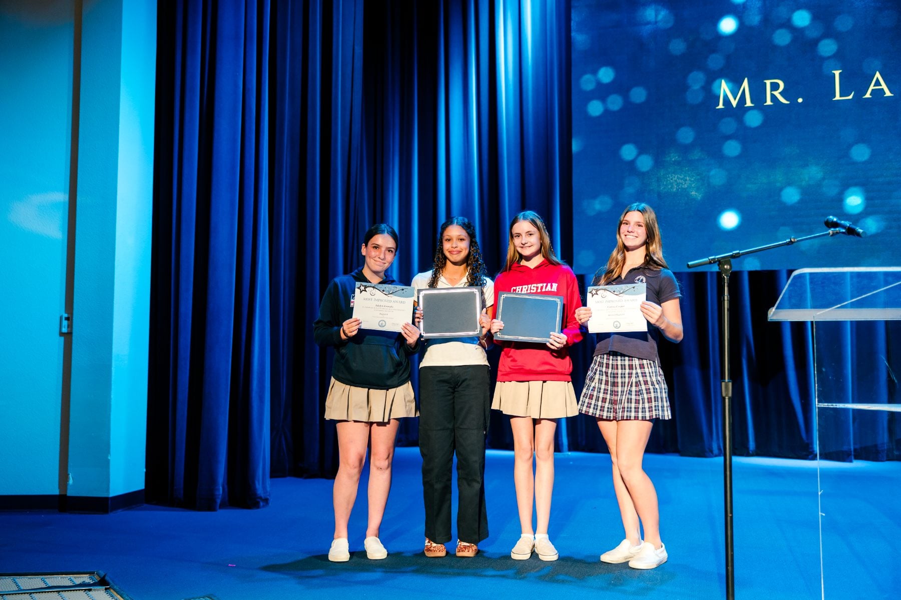 Four students hold certificates on stage during the Jr. High Awards Chapel