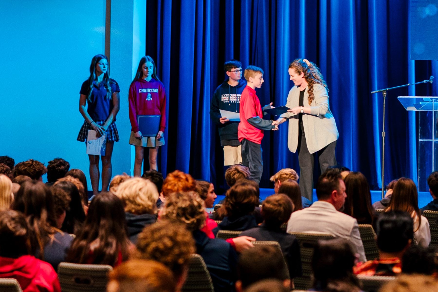 A teacher hands an award to a student during Christian junior high awards chapel.