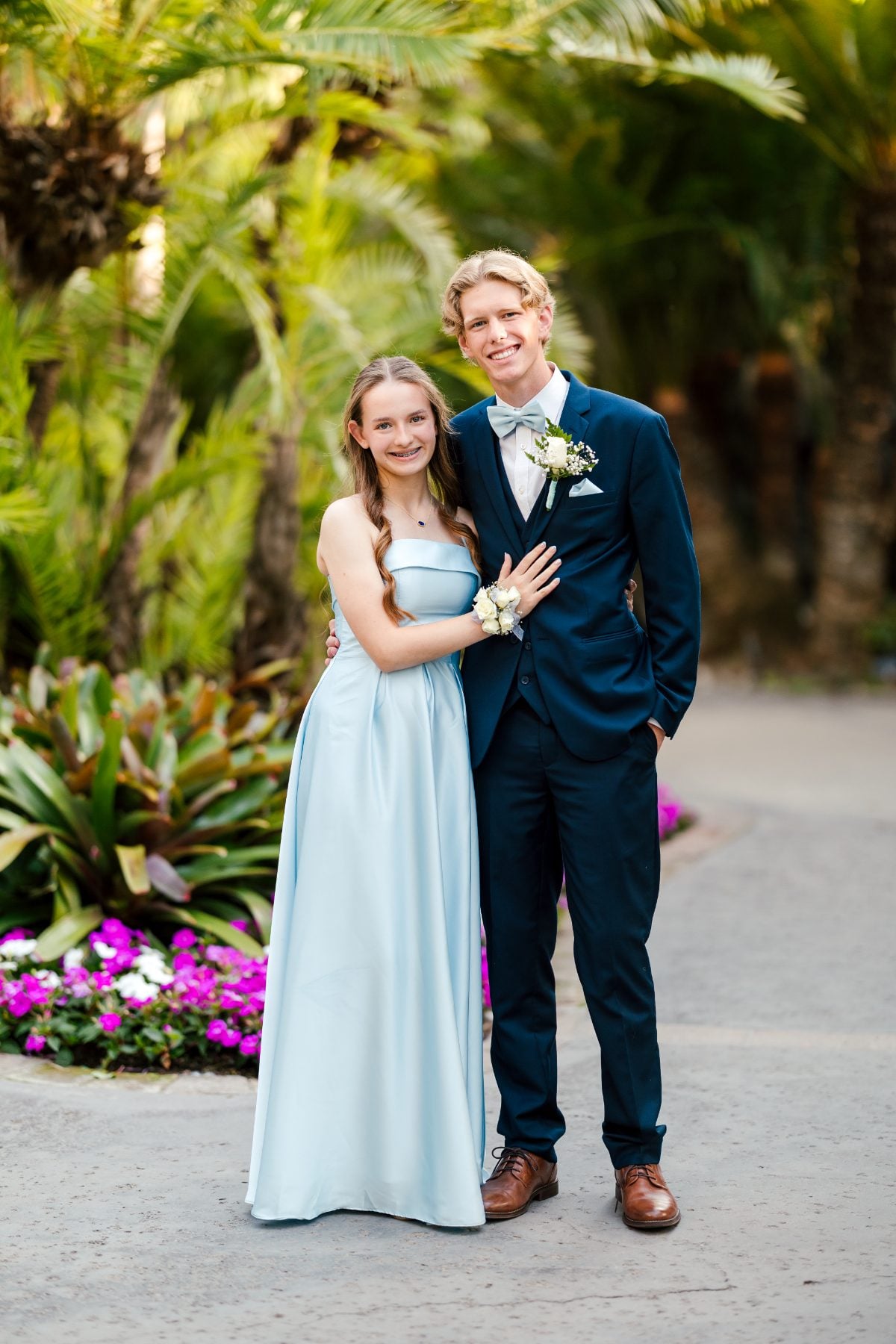 Student couple in light blue gown and navy suit pose in resort garden