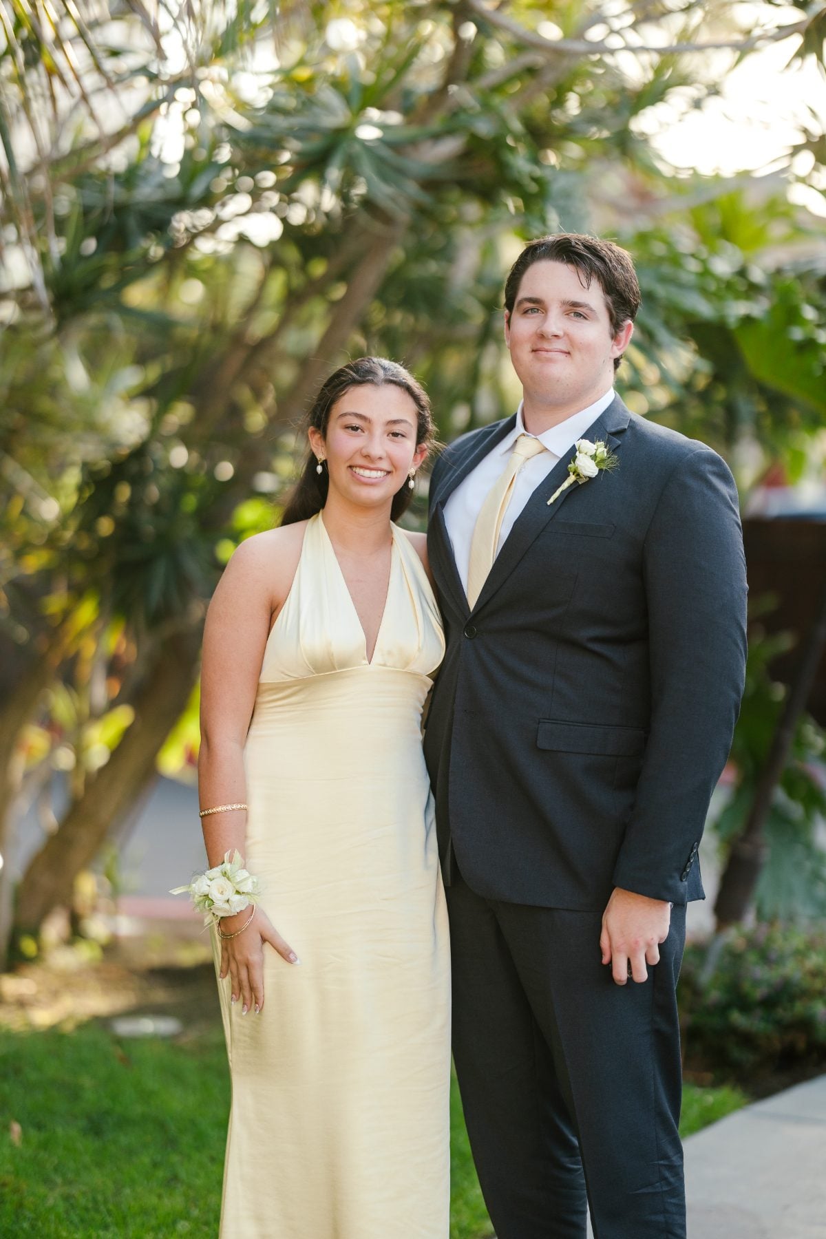 Student couple in yellow dress and dark suit pose among palm trees
