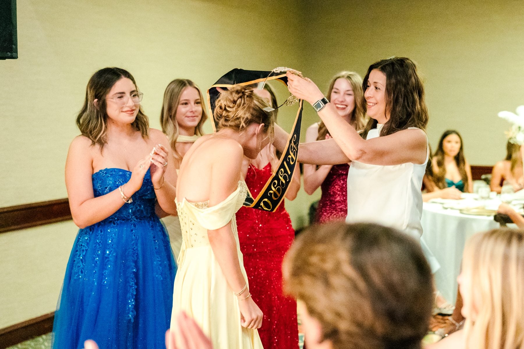 Students place sash on Jr/Sr Banquet queen as classmates celebrate nearby
