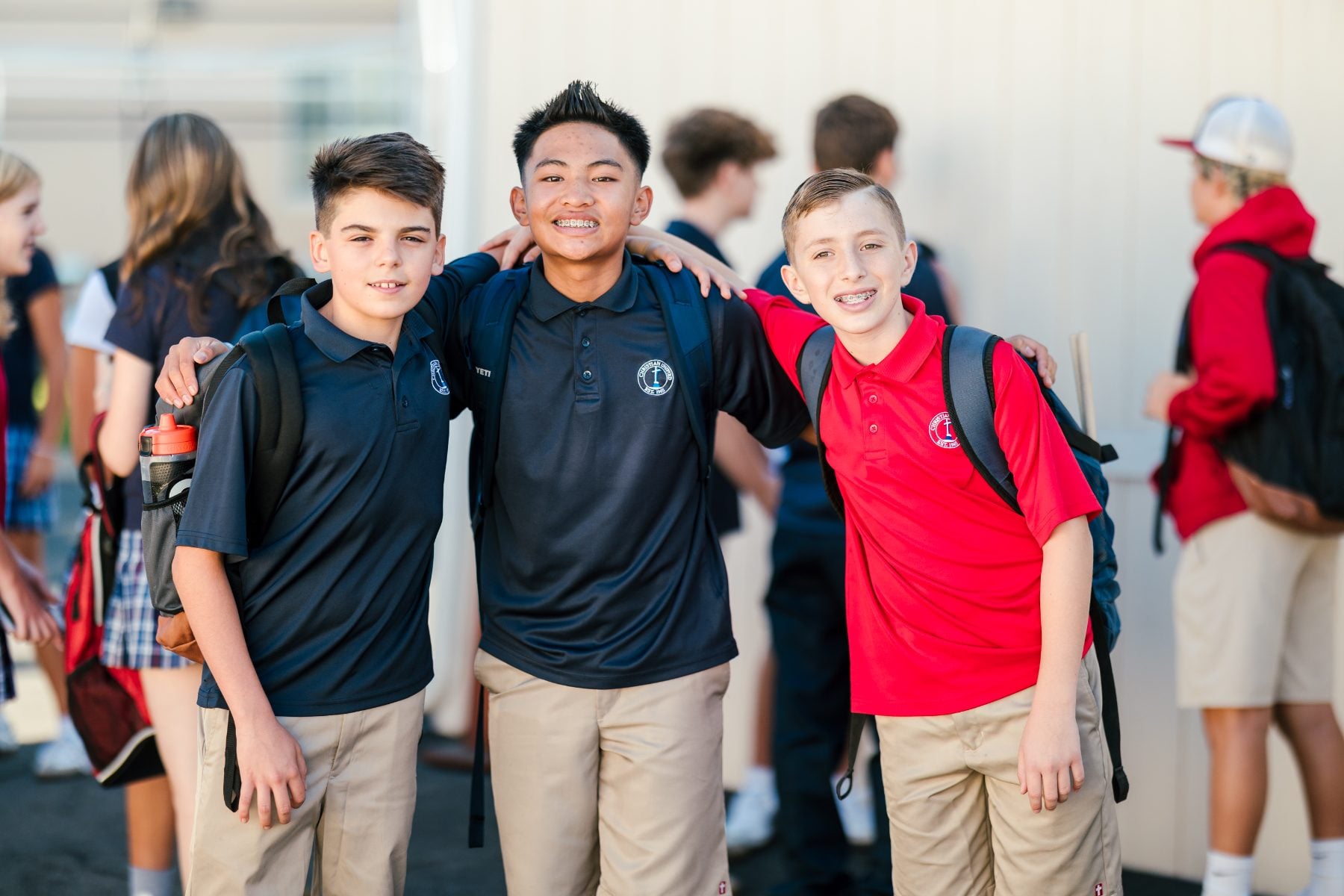 Three junior high boys stand arm in arm smiling outside campus