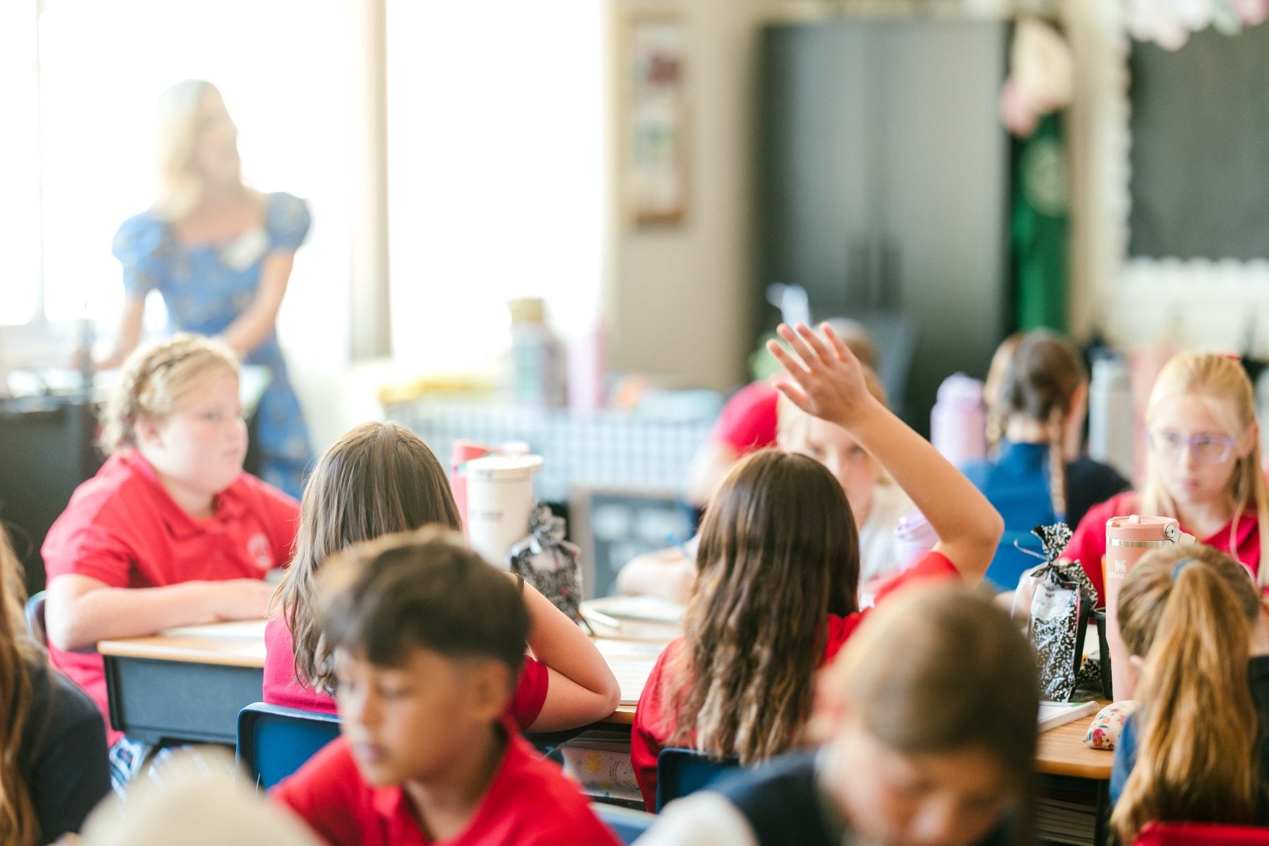 Junior high students sit at desks as a girl raises her hand