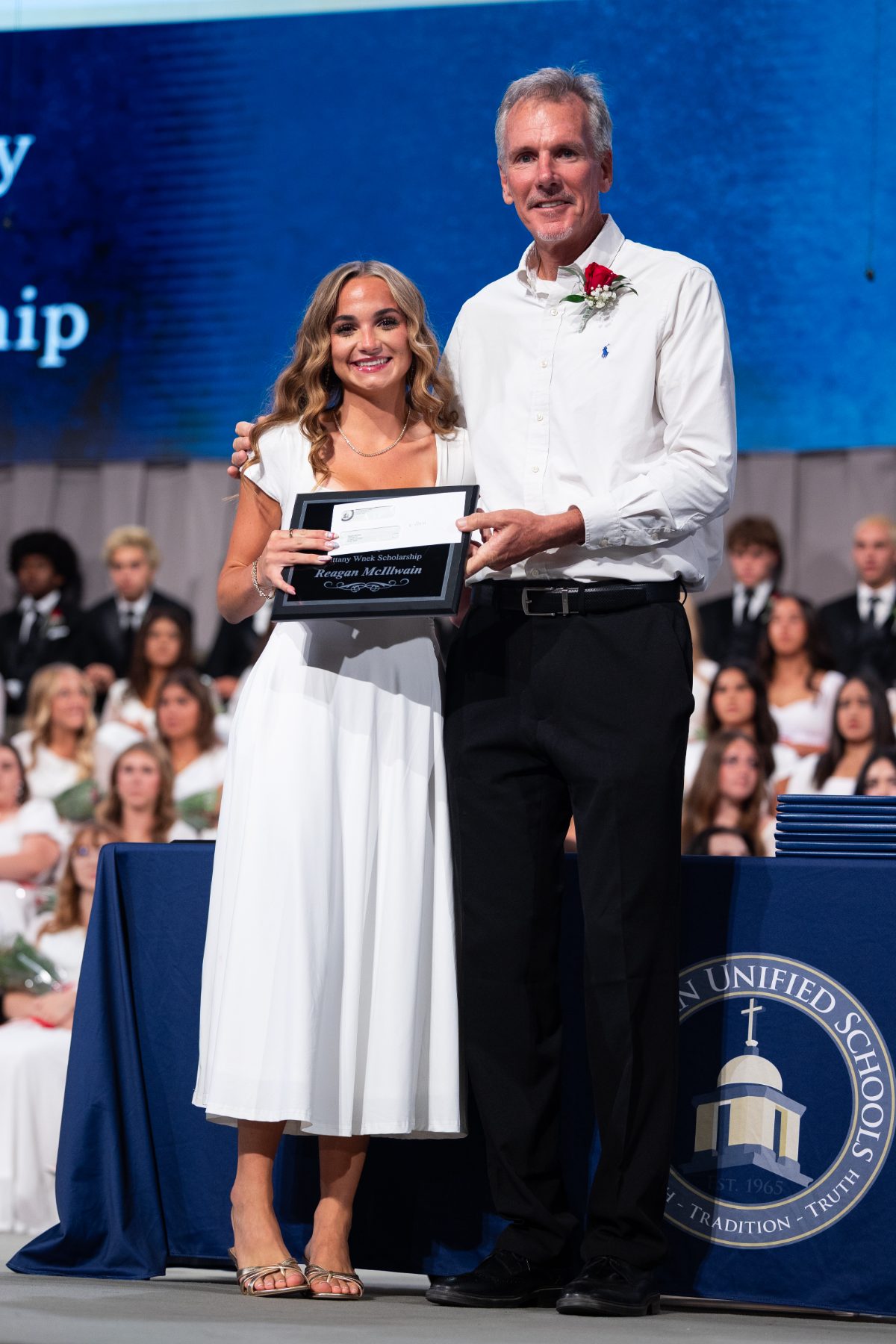 A private school graduate receives a scholarship award from a man in a blue shirt