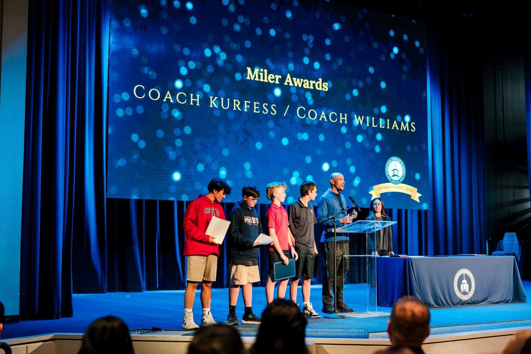 Students receive Miler Awards from coaches on stage at Shadow Mountain Event Center