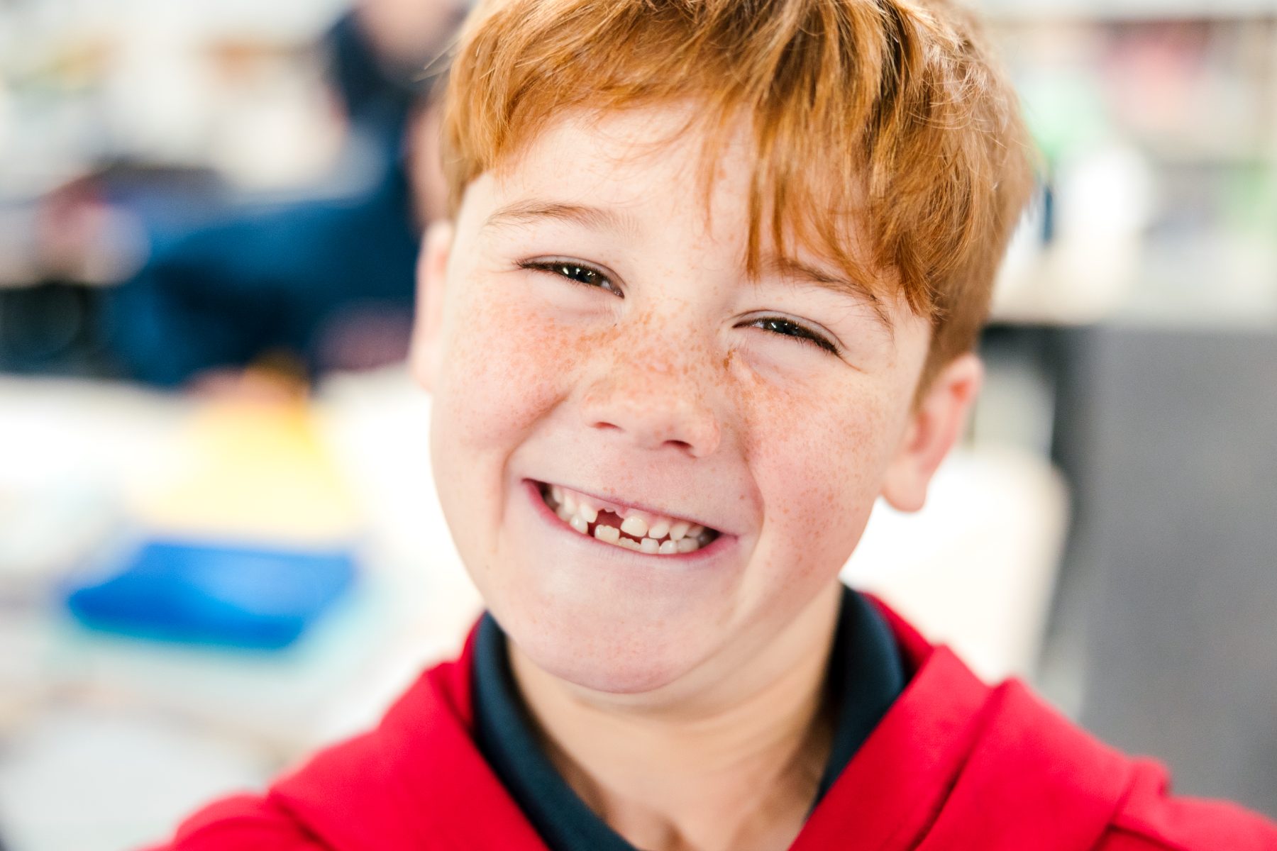 A red-haired boy grins widely showing a missing tooth in class