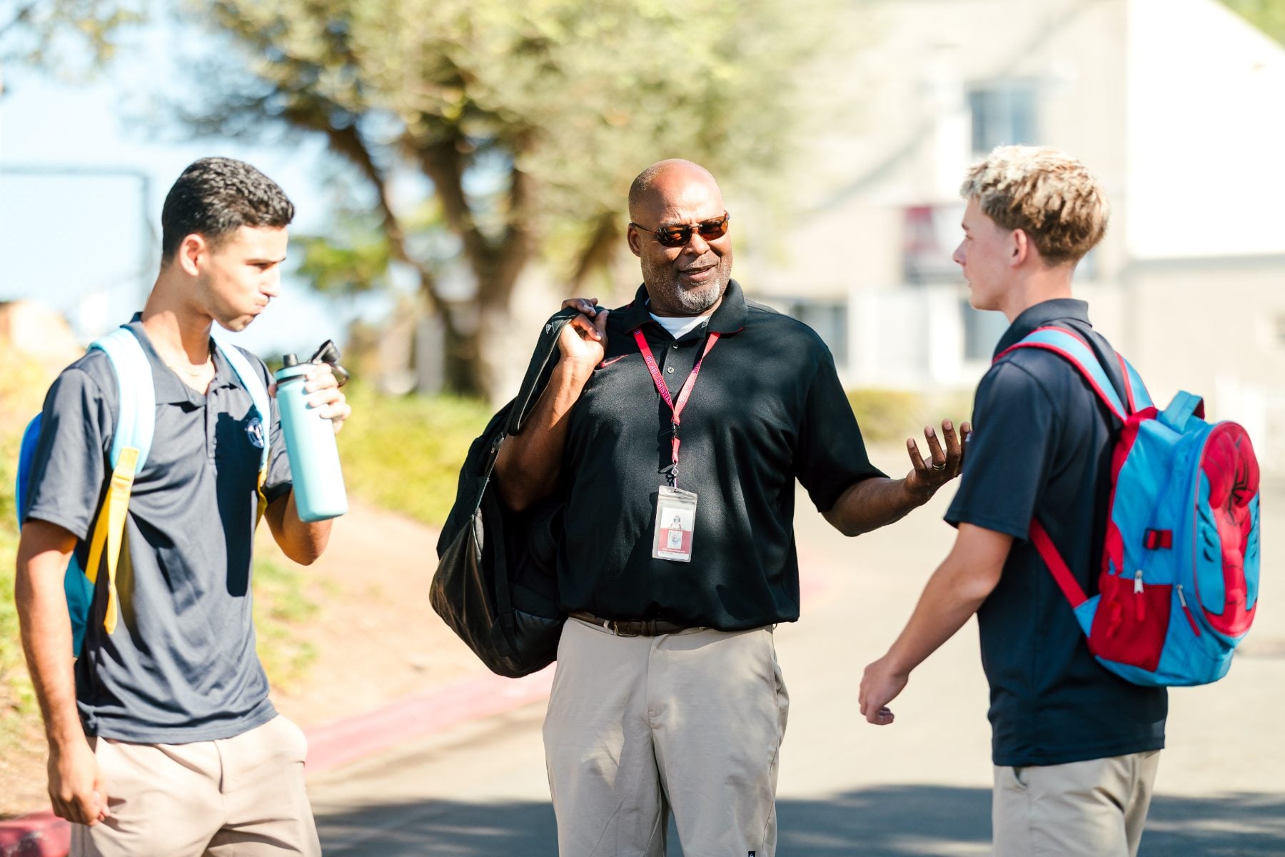 Staff member walks and chats with two students carrying backpacks outside