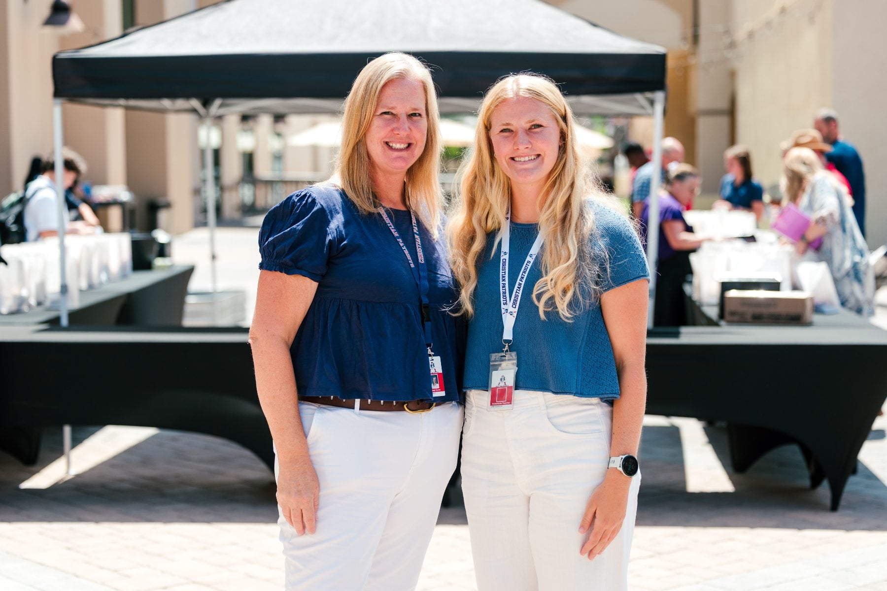Two Christian Unified Schools staff members smile together outside the event tent