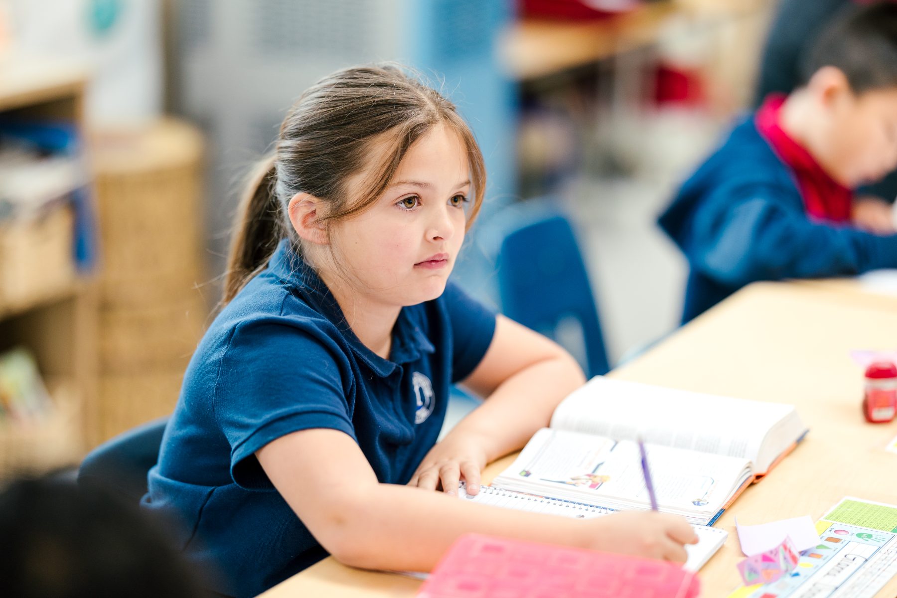 A student focuses on her assignment at a classroom desk