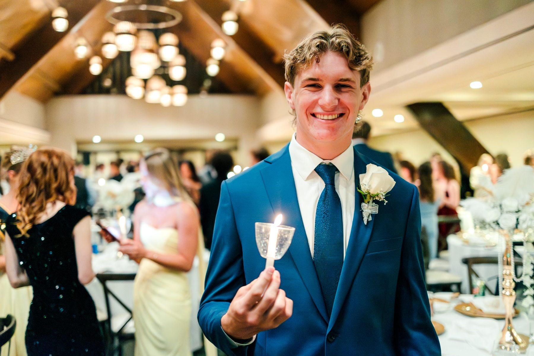 A student in a navy suit holds a lit candle smiling