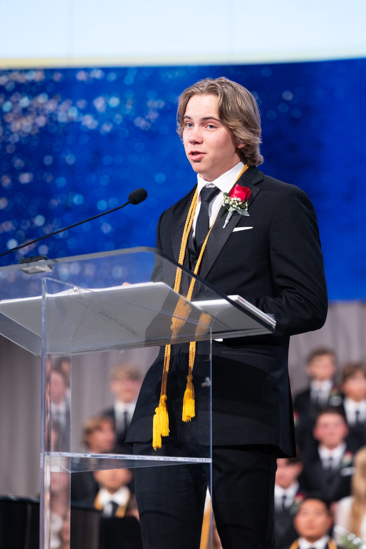 A student in gold cords speaks at the podium during commencement remarks