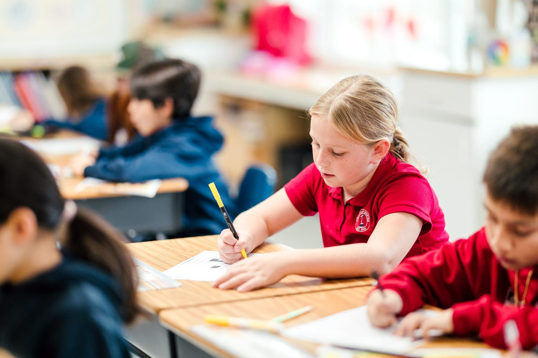 A student in a red polo writes at her desk during class at Christian Elementary School