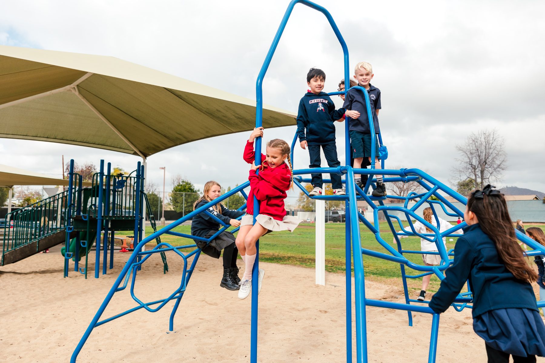 Students climb a blue playground structure together at recess