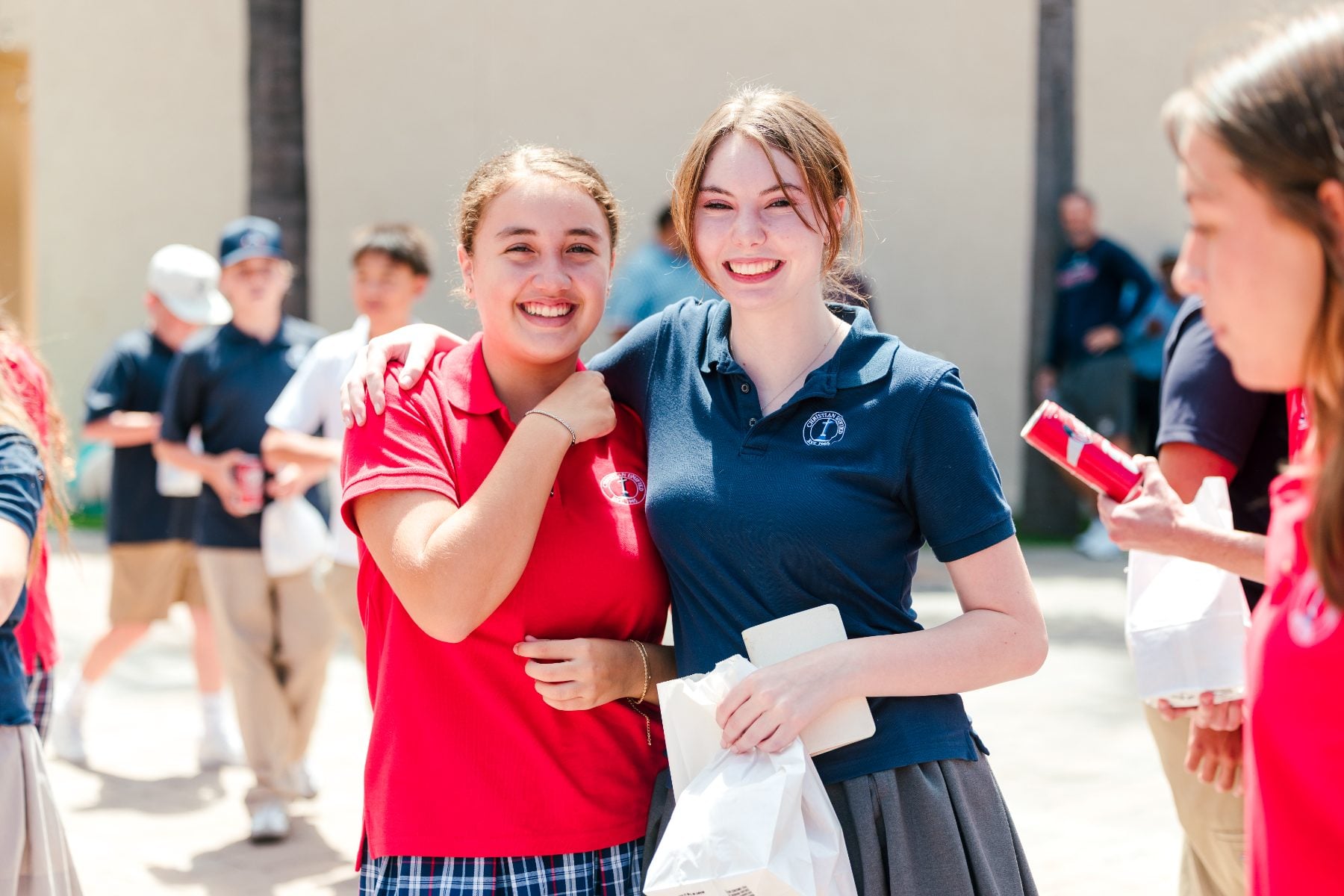 Two Christian Unified Schools students embrace and smile outdoors on campus