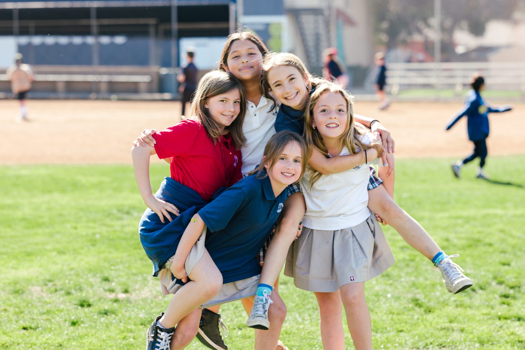 Five elementary students pile together laughing on the field during recess