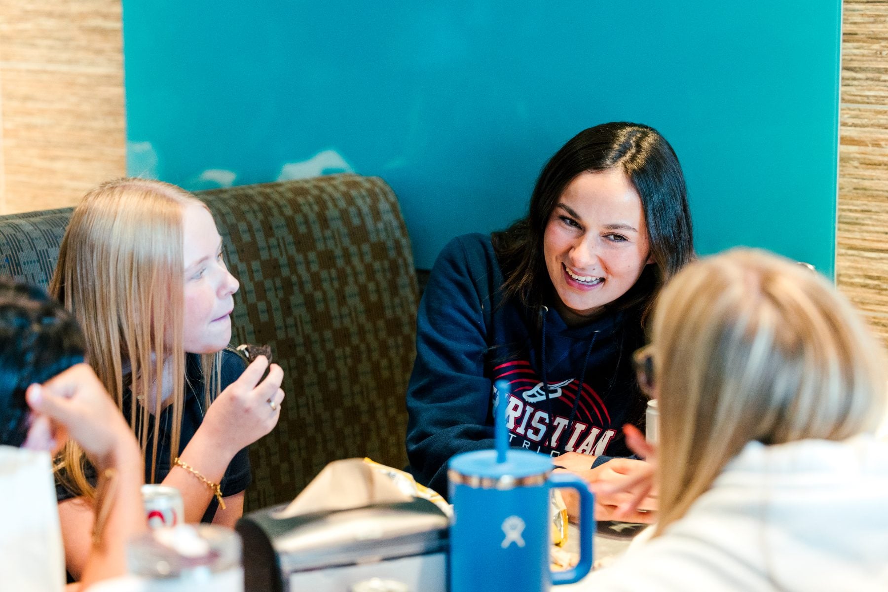 Three students chat and laugh together at a booth table