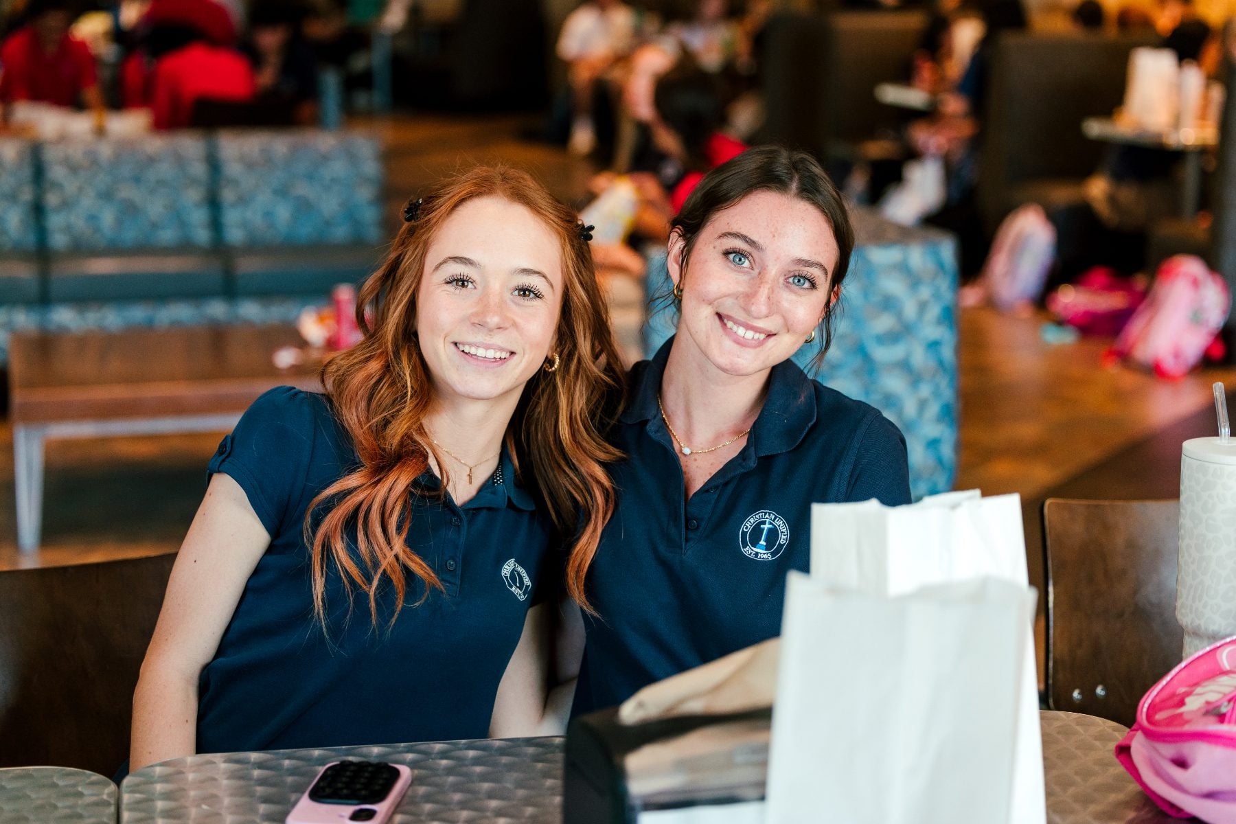 Two students in navy polos smile together at the BBQ event