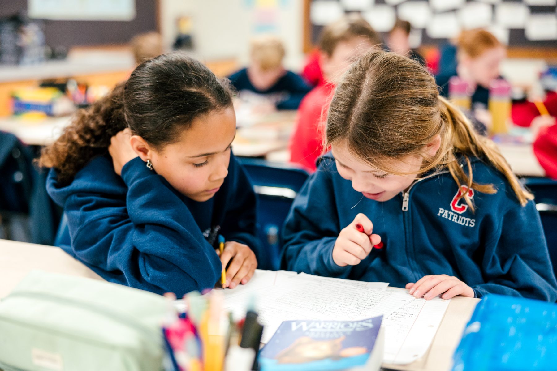 Two students in Patriots sweatshirts work together on a classroom assignment
