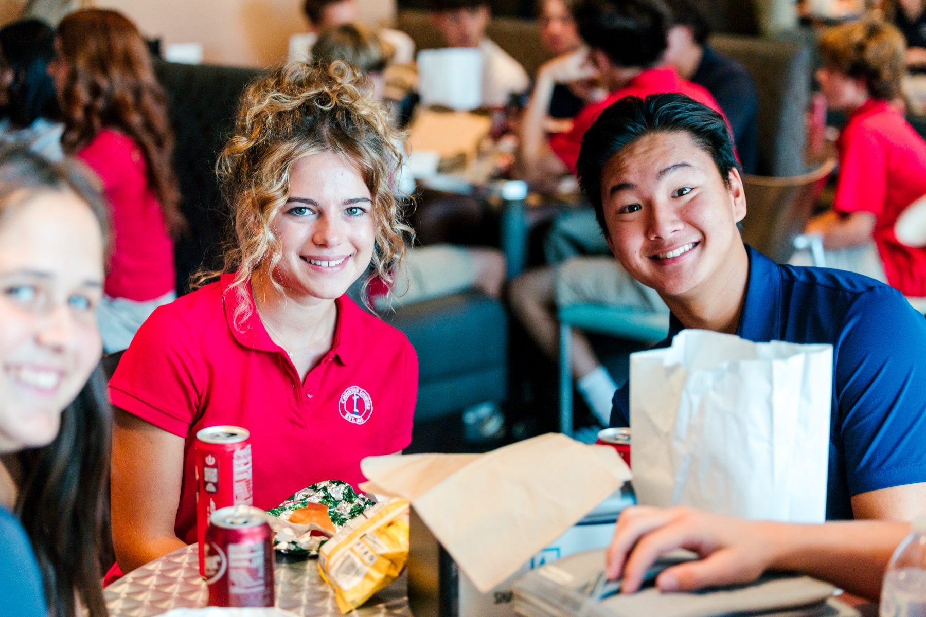 Three students in red polos share a laugh over lunch