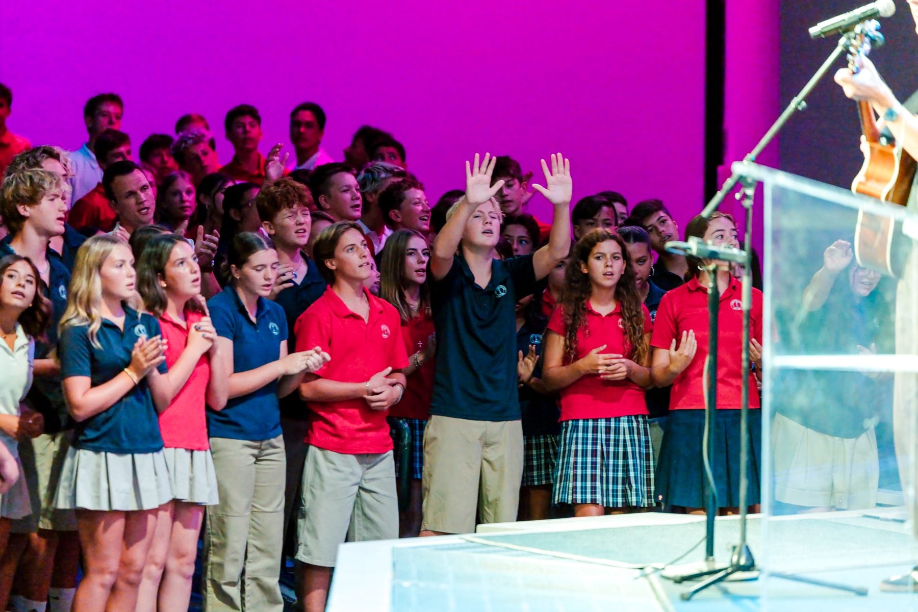 Students in uniform sing with hands raised during chapel worship