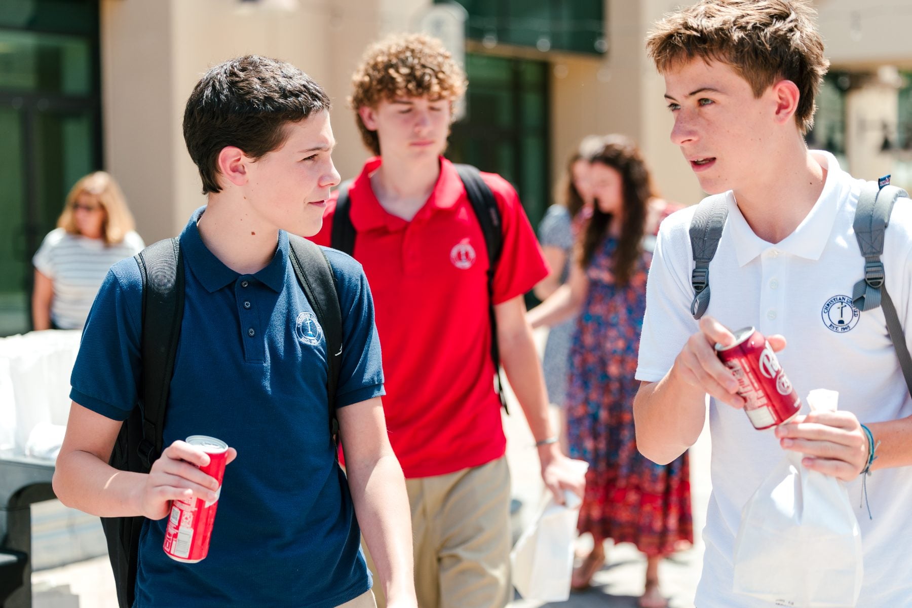 Two students walk and talk holding soda cans after the BBQ