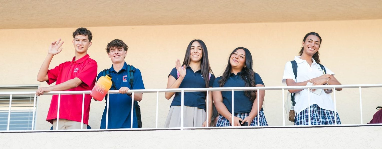 Five students line a balcony railing, waving on the first day of school