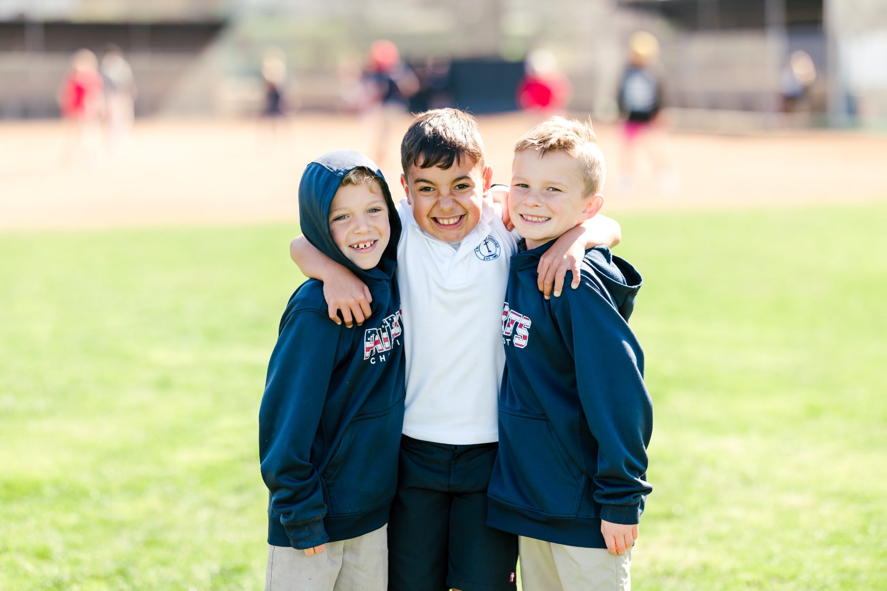 Three students in Patriots hoodies smile together on the field