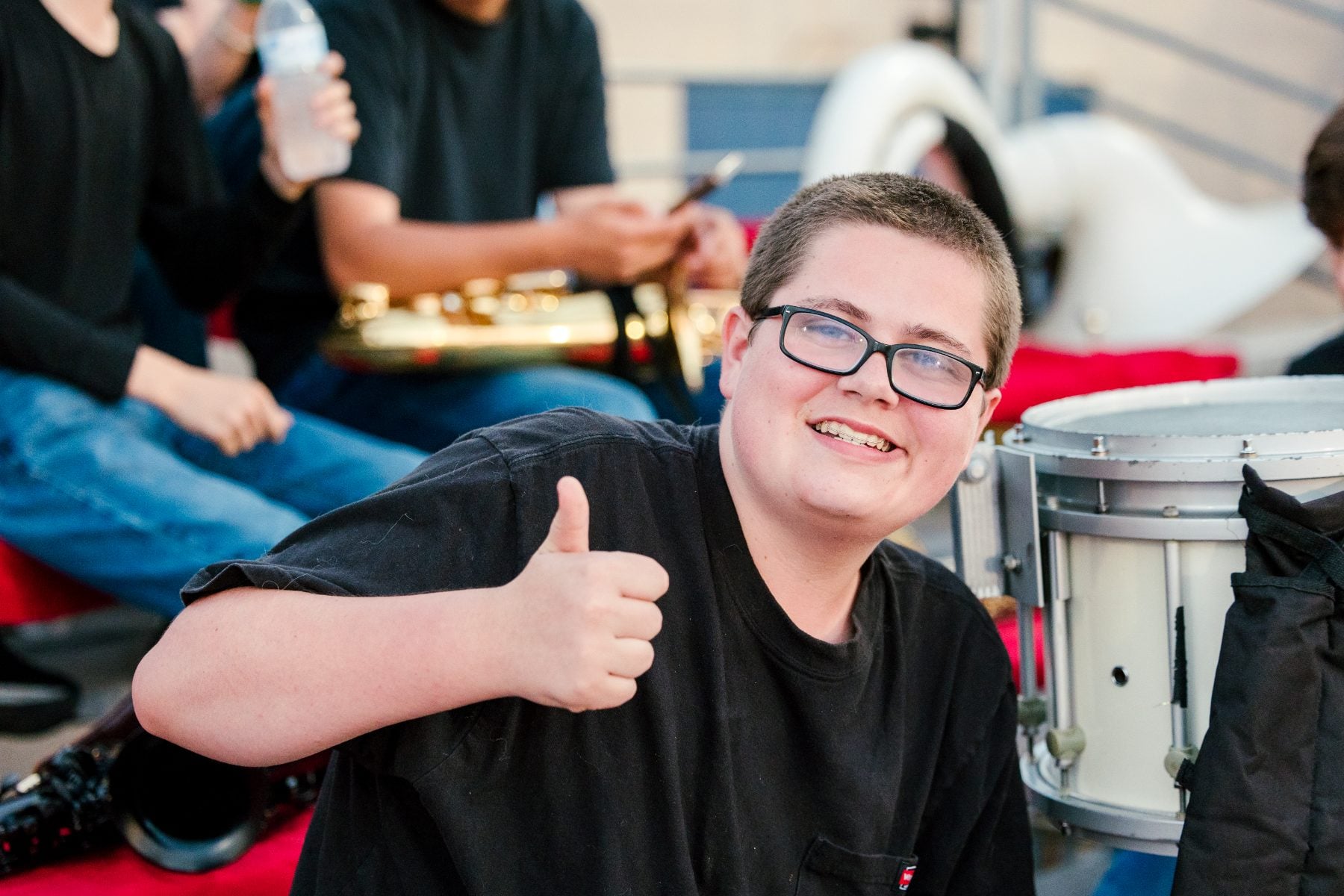 A young band member gives a thumbs up beside the drum section